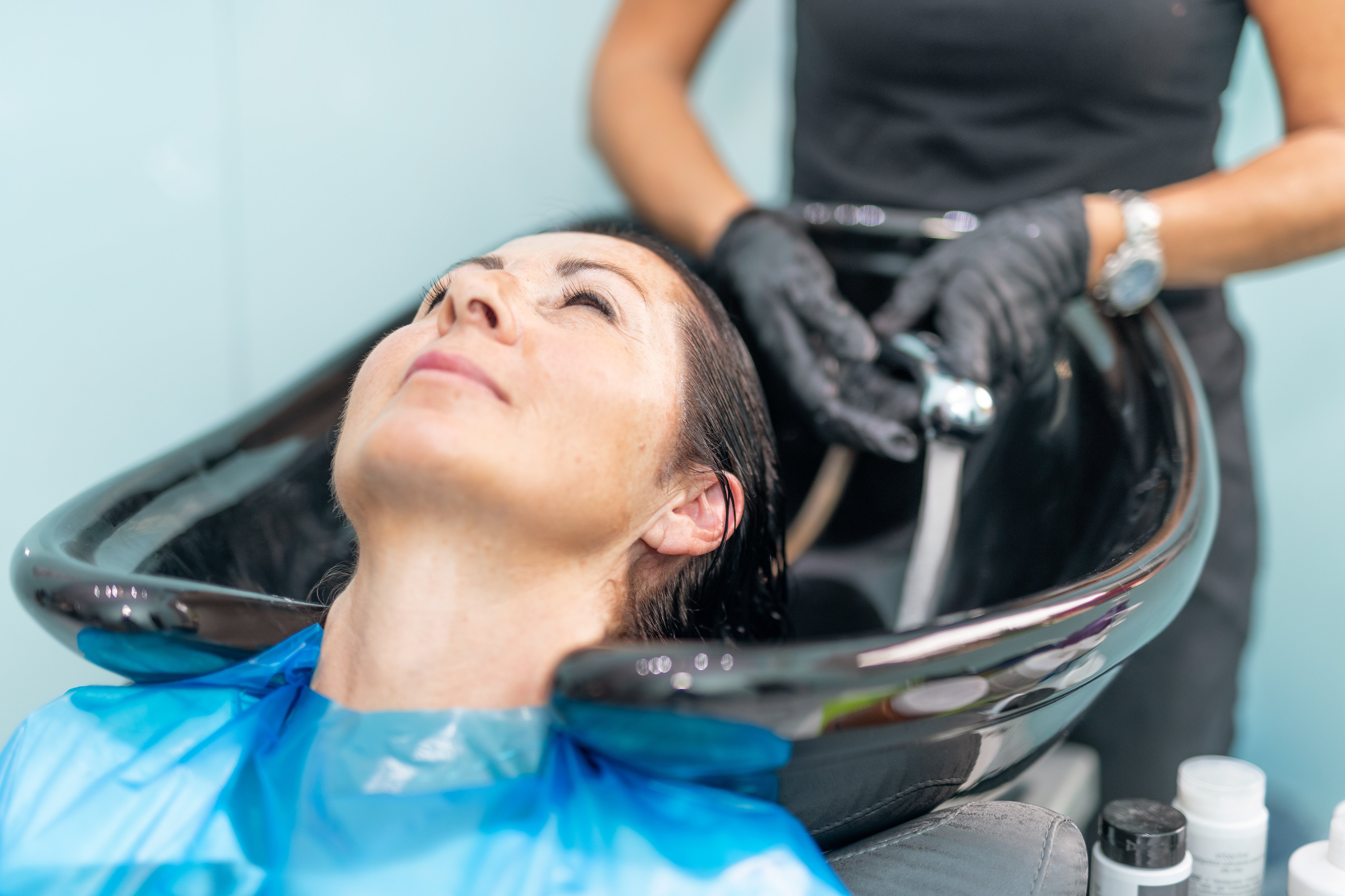 Glückliche Frau mit Friseur, die ihren Kopf am Friseursalon wäscht. | Quelle: Shutterstock