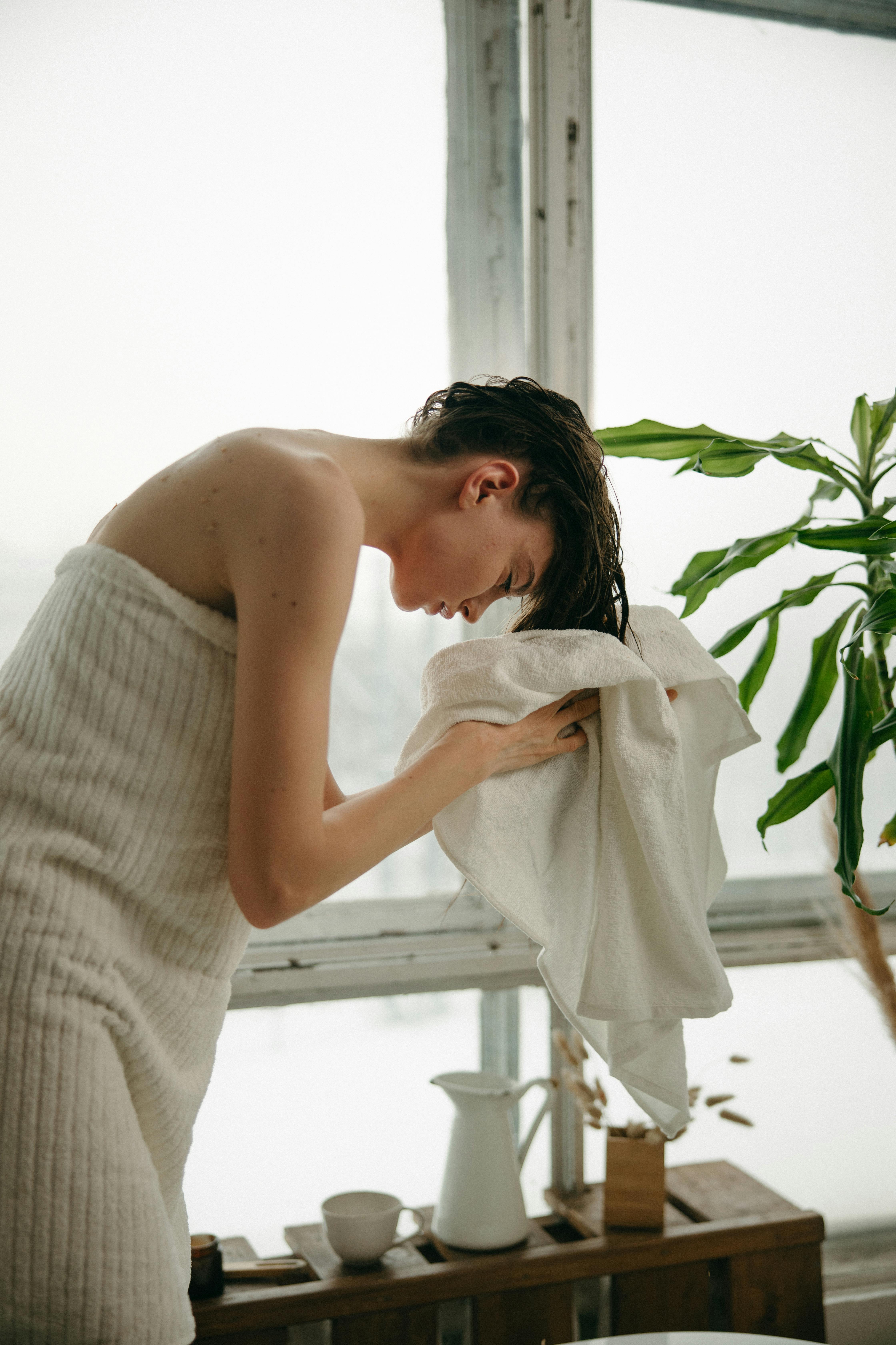 A woman drying her hair with a towel after showering | Source: Pexels