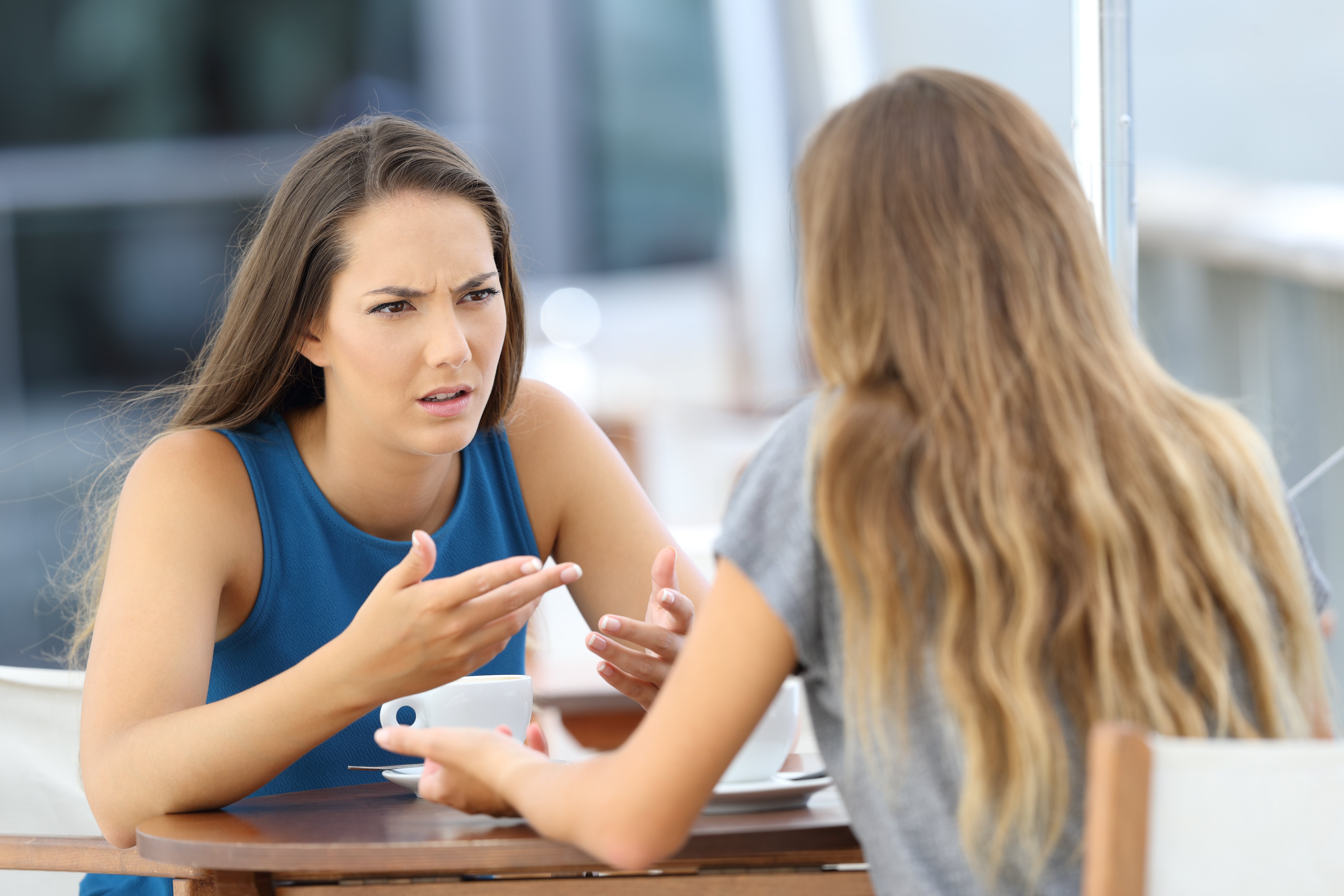Zwei wütende Frauen, die ernsthaft reden und in einem Café sitzen | Quelle: Shutterstock