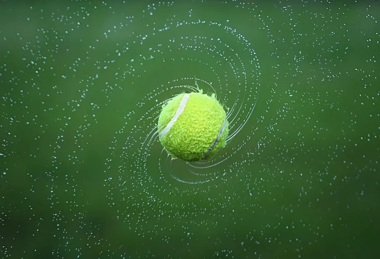 Une balle de tennis mouillée qui tourne dans les airs | Photo : Pixabay/Bessi