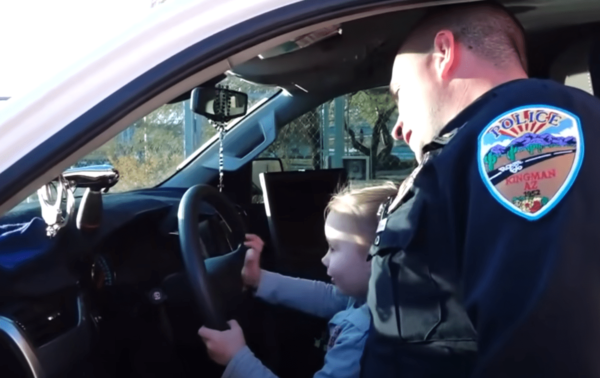 A little girl sits on her adoptive father's lap in a police vehicle | Photo: Youtube/Inside Edition
