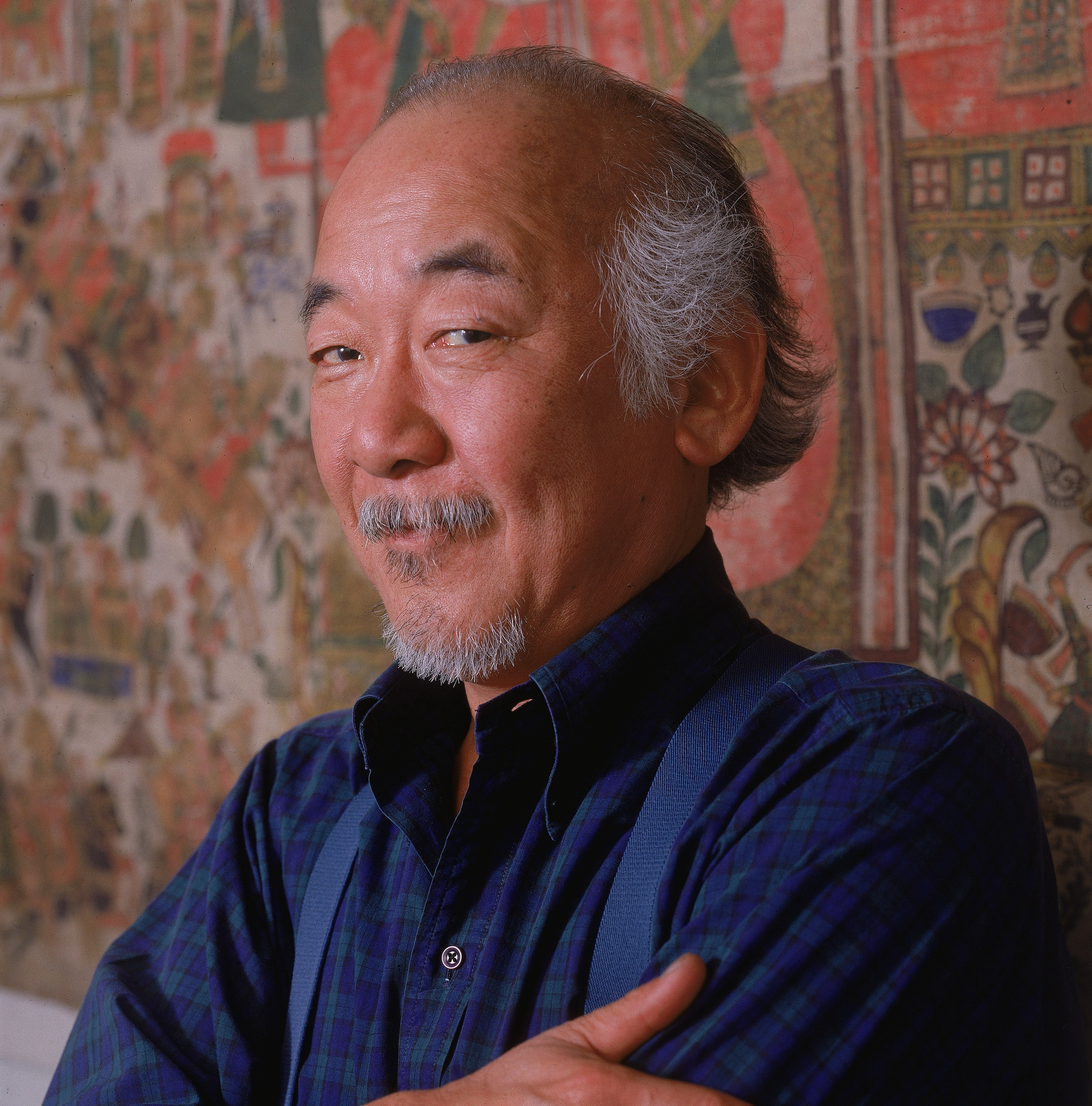 Comedian Pat Morita posing while standing against a tapestry, 1988. | Source: Getty Images