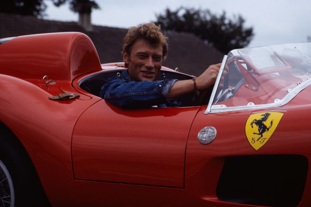 Le chanteur et acteur français Johnny Hallyday au volant d'une Ferrari 250 GT Testarossa décapotable rouge. | Photo : Getty Images