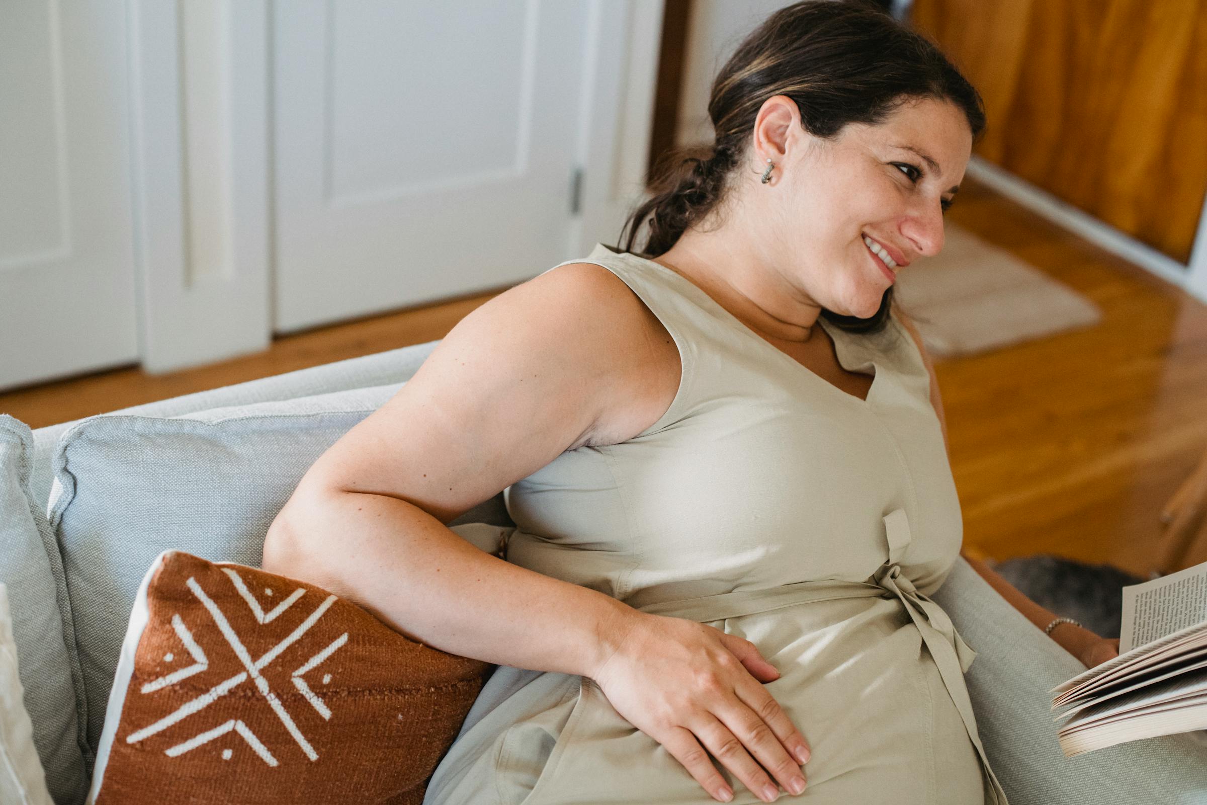 A pregnant woman smiling and sitting on a couch | Source: Pexels
