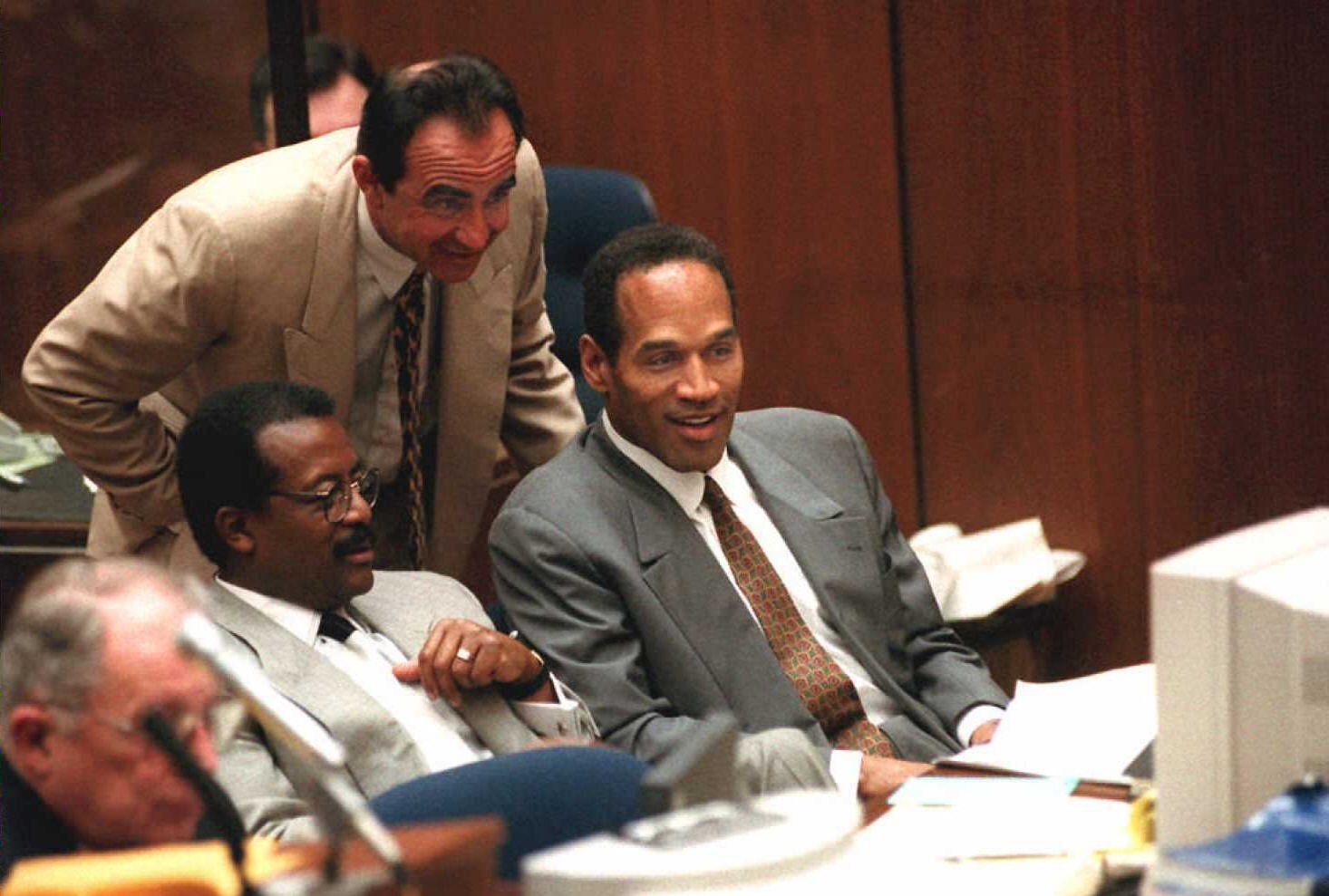 O.J. Simpson (C) smiles with his attorneys Robert Shapiro (standing) and Johnnie Cochran Jr as they view a video tape on February 6 | Source: Getty Images