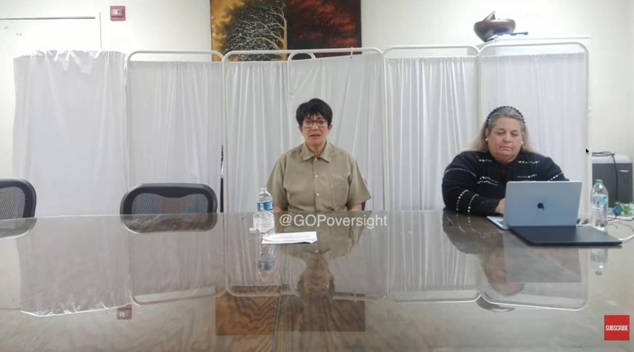 Under the Microscope: Maxwell is flanked by officials and boxed in by stark white privacy screens during her testimony. Her tightly controlled posture and blank expression have sparked outrage, as viewers accuse her of showing no remorse while stonewalling Congress. | Source: YouTube/New York Post