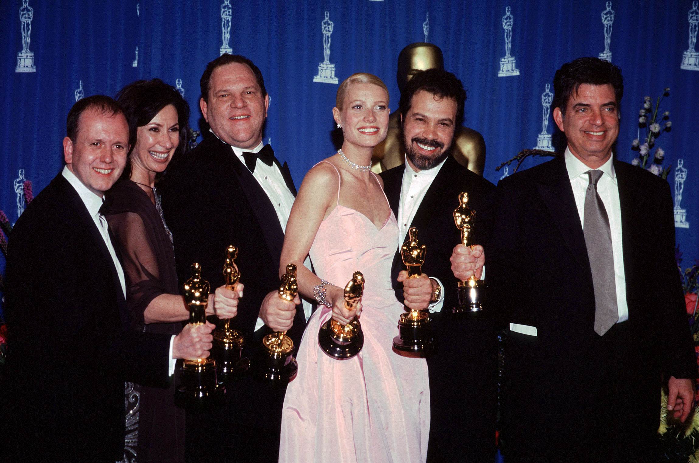 From (L-R) David Parfitt, Donna Gigliotti, Harvey Weinstein, Gwyneth Paltrow, Edward Zwick, and Mark Norman pose in the pressroom at the 71st Annual Academy Awards on March 21, 1999 in Los Angeles, California. | Source: Getty Images