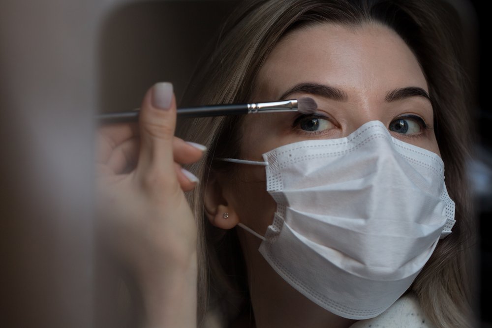 Mujer usando mascarilla mientras maquilla sus ojos. | Foto: Shutterstock