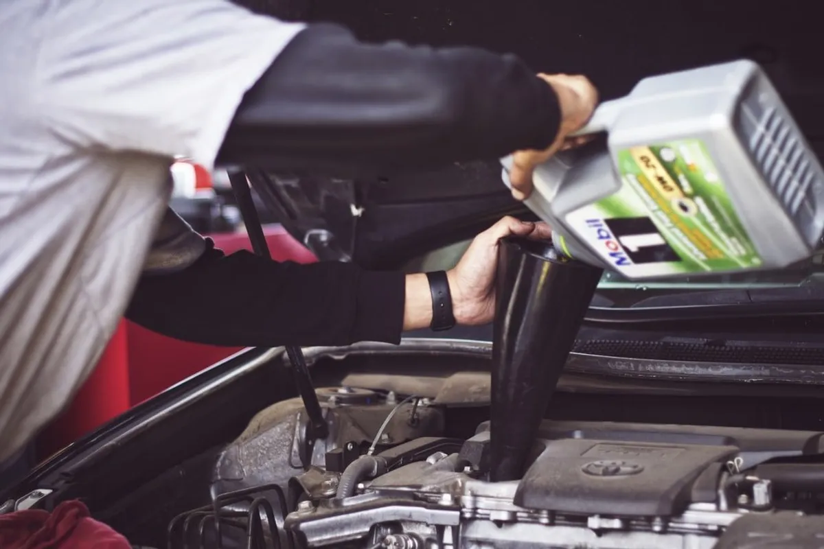 Un homme versant de l'huile dans un moteur de voiture | Source : Unsplash