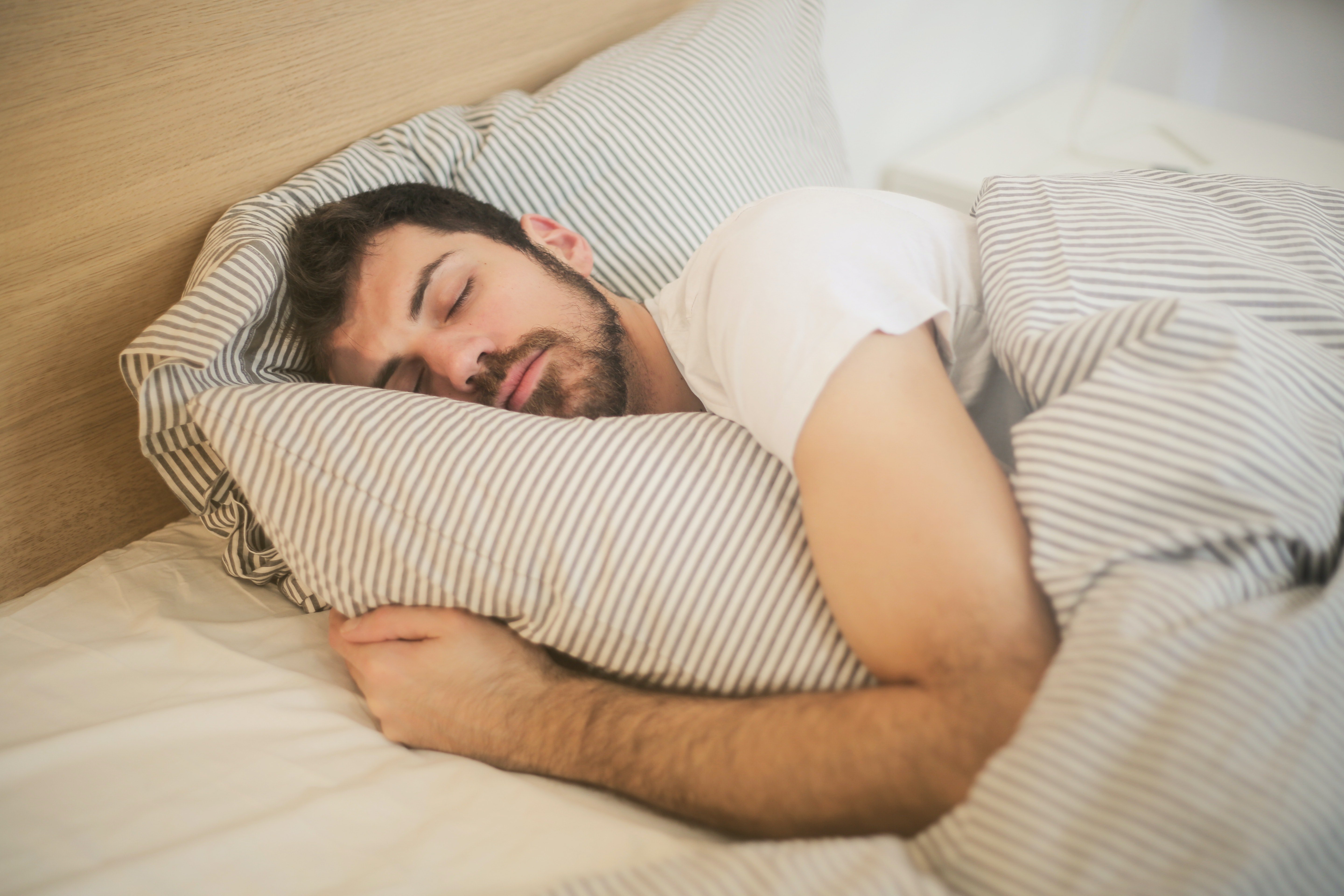 Un hombre abrazando una almohada mientras duerme. | Foto: Pexels