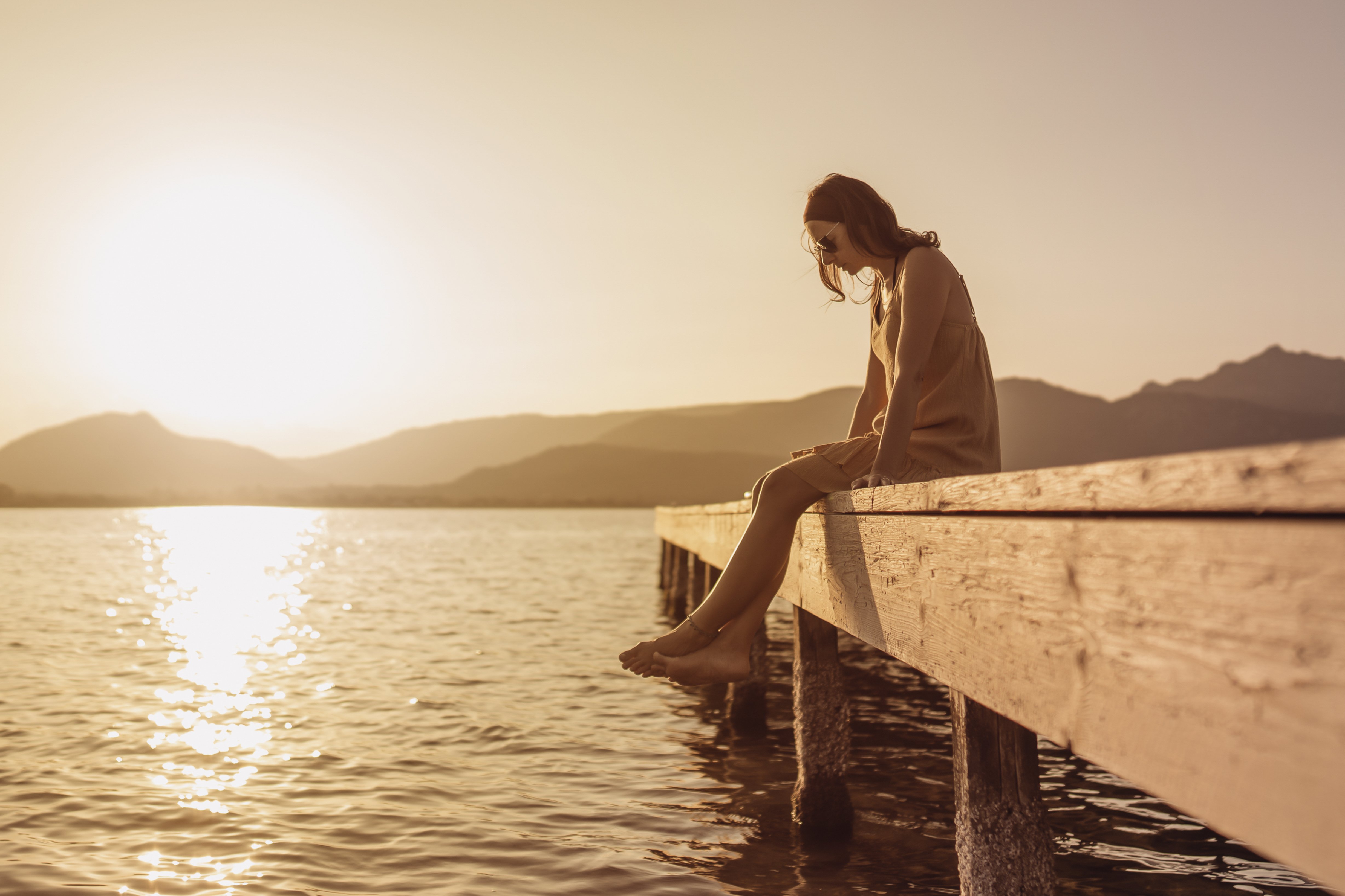 A young woman sitting on a pier at sunset.│ Source: Shutterstock