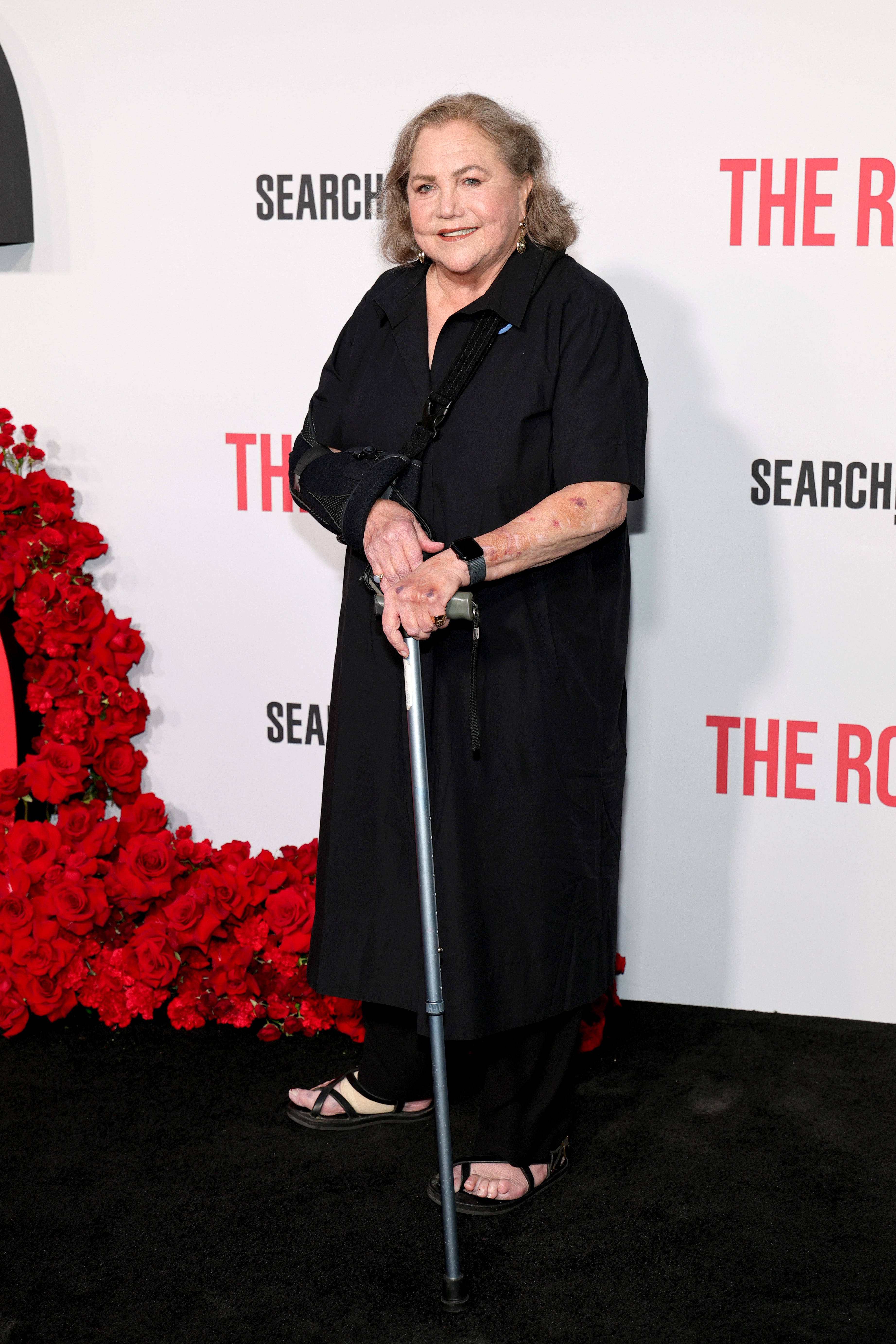 Dressed in a flowing black ensemble and using a cane, Kathleen Turner radiates resilience and timeless grace as she poses on the red carpet of Searchlight Pictures' "The Roses" New York Premiere.