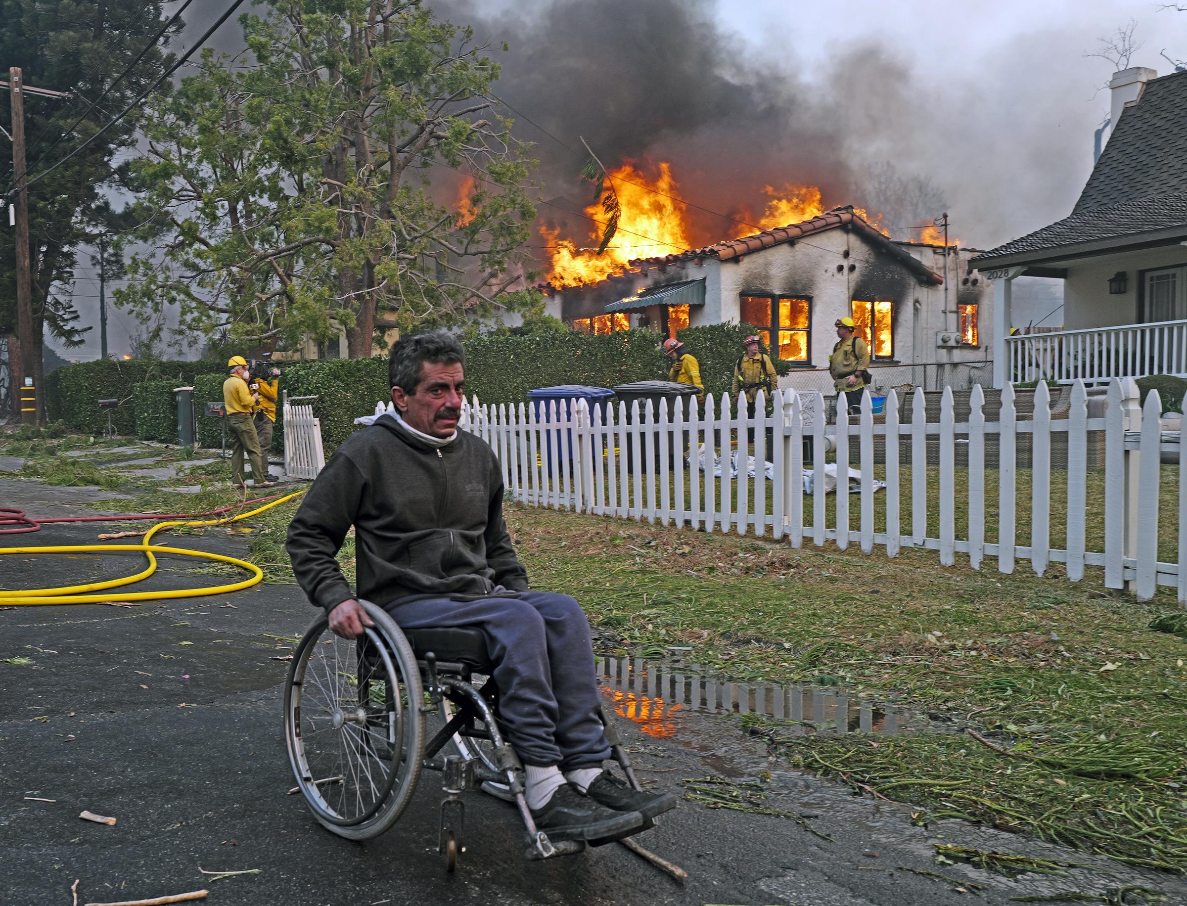 A man in a wheelchair goes past a house on fire from the Eaton Fire in the Altadena neighborhood on January 08, 2025, in Pasadena, California | Source: Getty Images