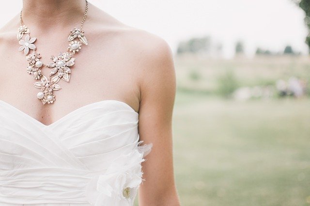Woman in wedding dress with flowered peal necklace stands outside | Photo: Pixabay