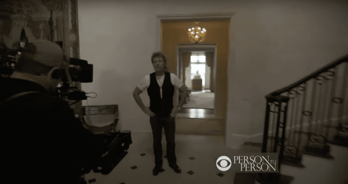 Record producer Jon Bon Jovi standing in his hallway next to the staircase. / Source: YouTube/@CBS