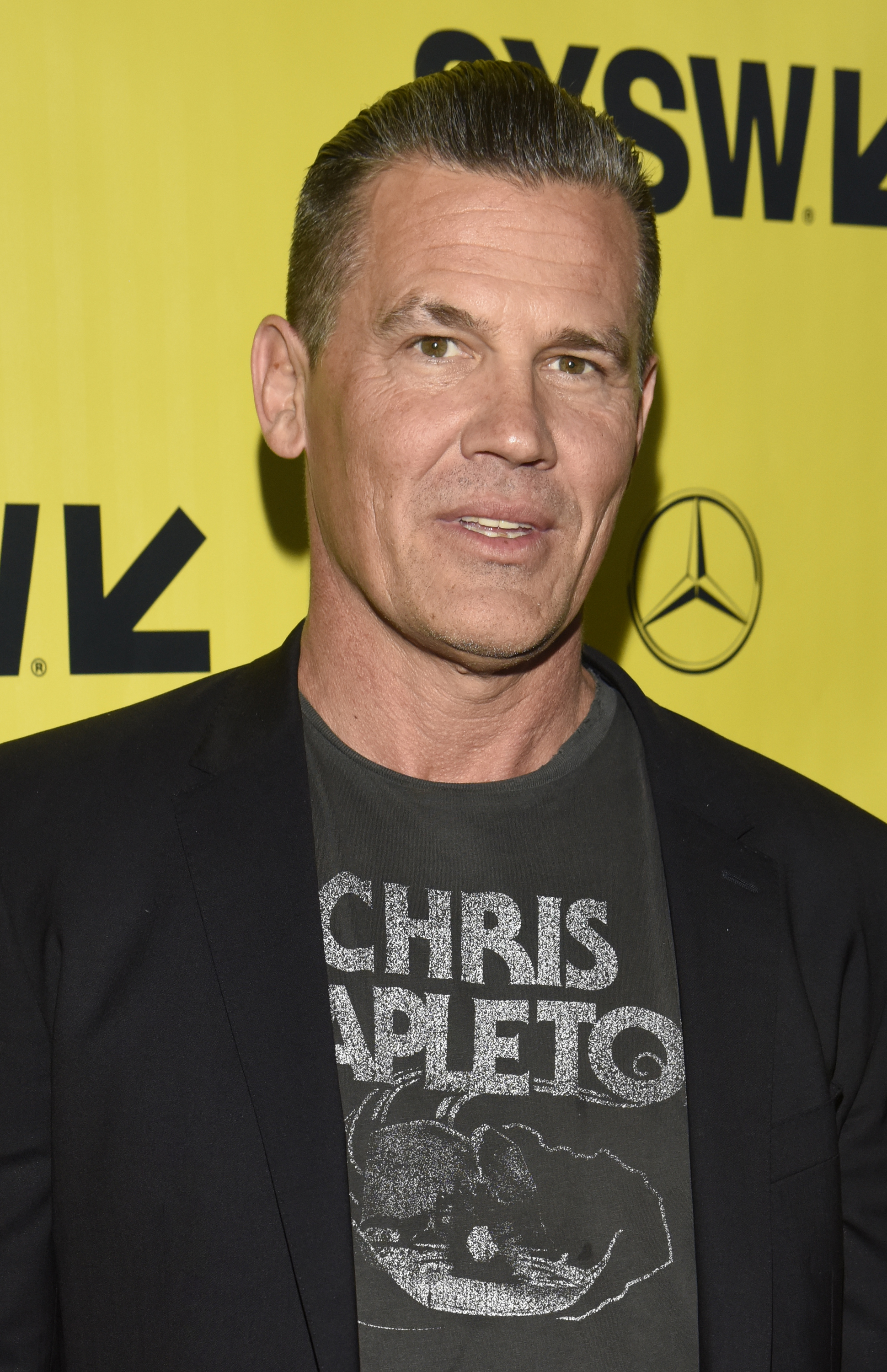 Wearing a graphic T-shirt under a black blazer, he appears clean-shaven with slicked-back hair and a noticeably fuller face — a casual look marking a shift away from formal red carpet styling.