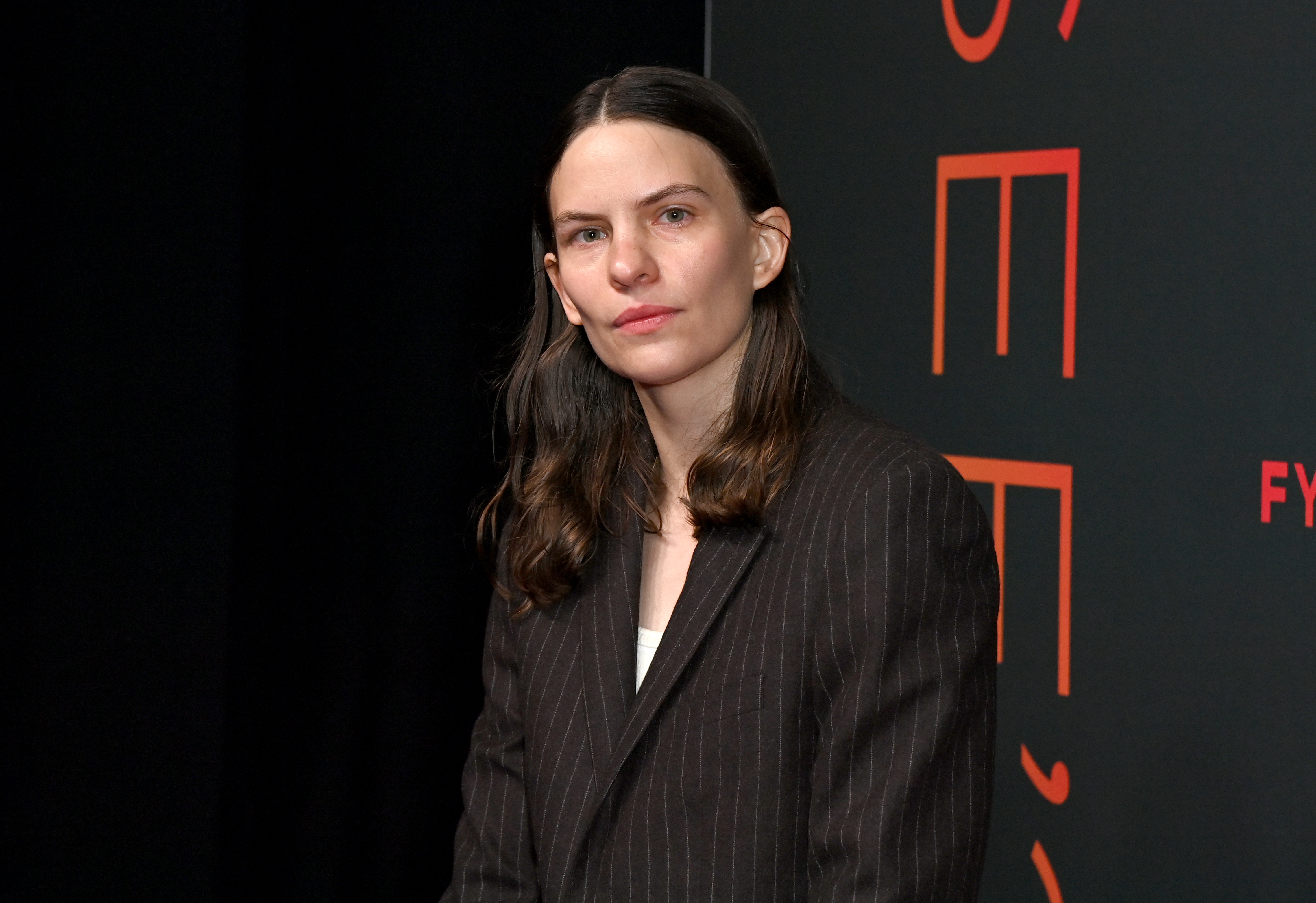 Eliot Sumner at the Netflix "Ripley" FYSEE screening in Los Angeles, May 2024 — dark hair pulled back, wearing a dark pinstripe blazer over a white top, the angular jawline and pale eyes strikingly familiar.