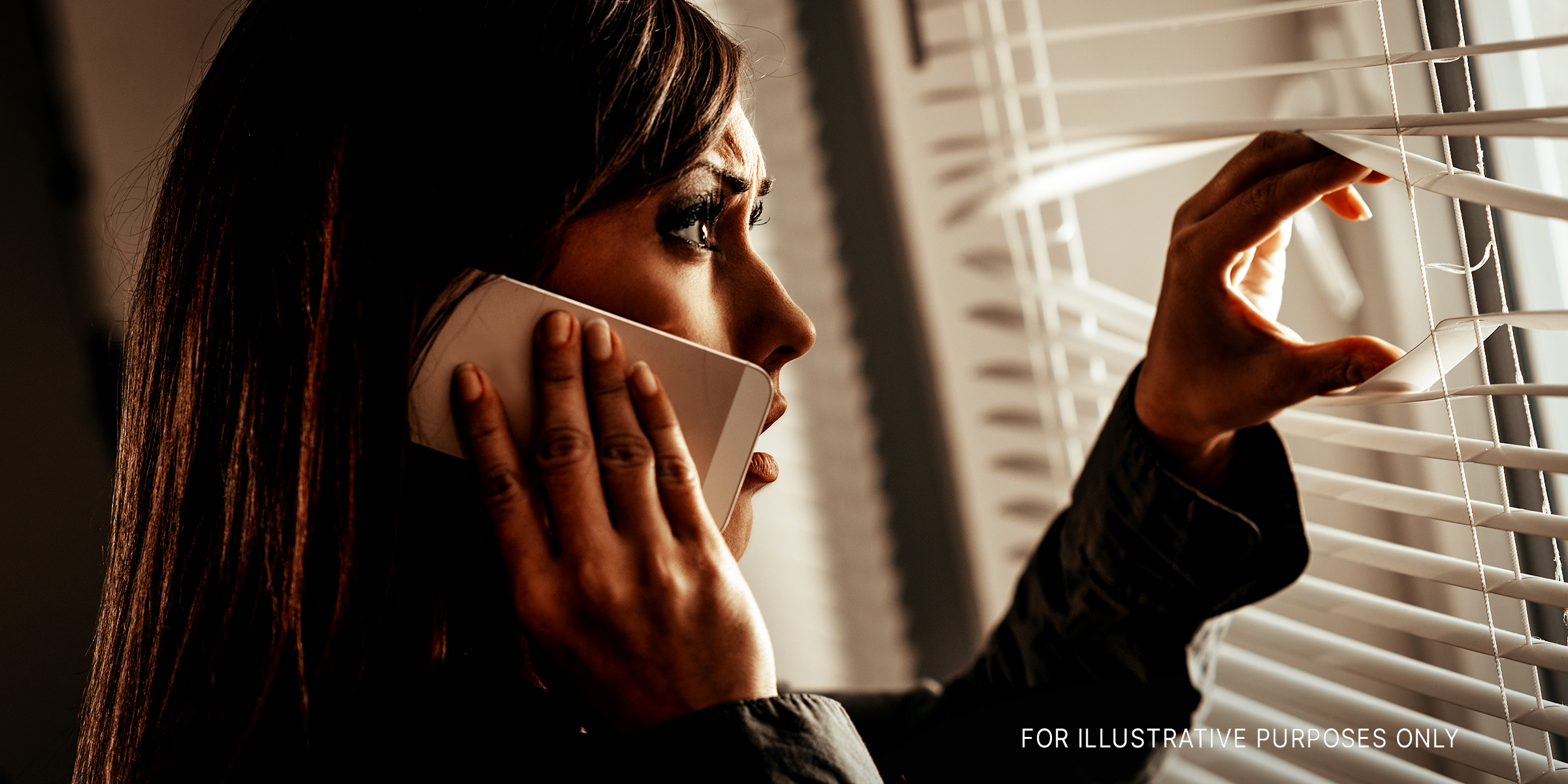 A woman looking out the window while holding her phone | Source: Shutterstock