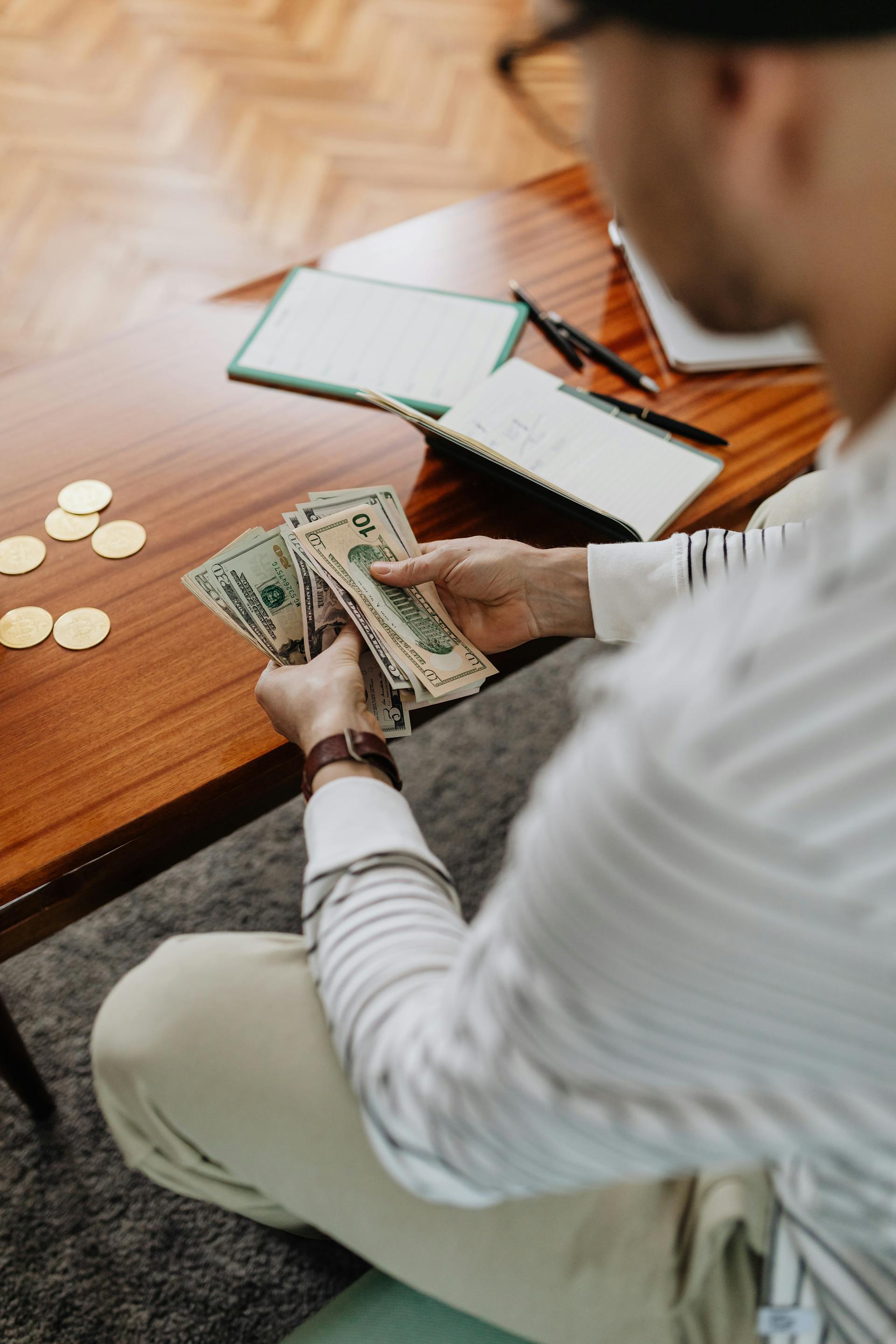 A person counting banknotes with a bunch of coins and notepads lying in front of him | Source: Pexels