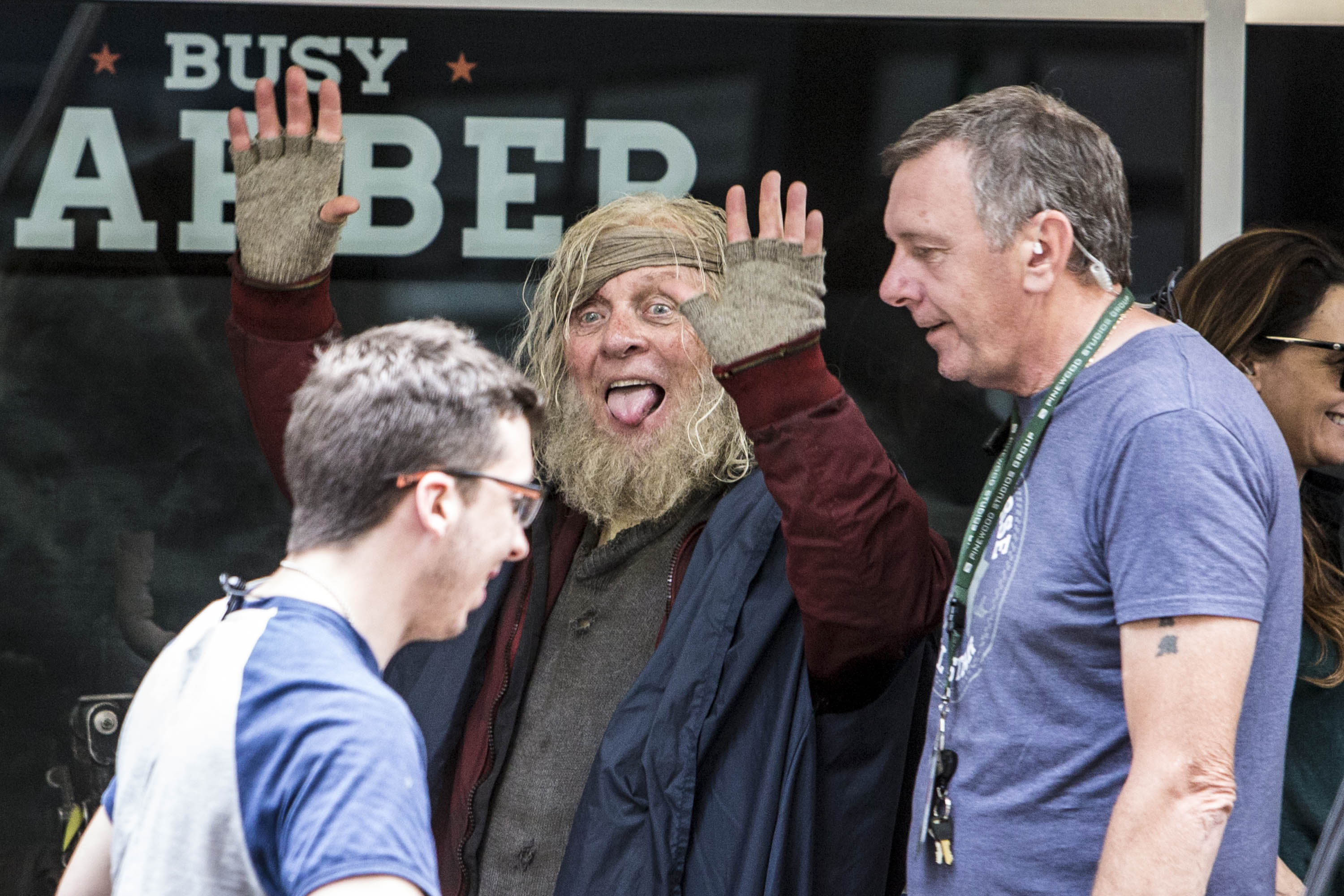 Anthony Hopkins, in rugged costume and unkempt beard, playfully raises his hands and sticks out his tongue on set. Surrounded by crew members, his lighthearted energy contrasts the intense world of "Thor: Ragnarok." The candid moment captures a legendary actor enjoying the craft behind the chaos of filmmaking.