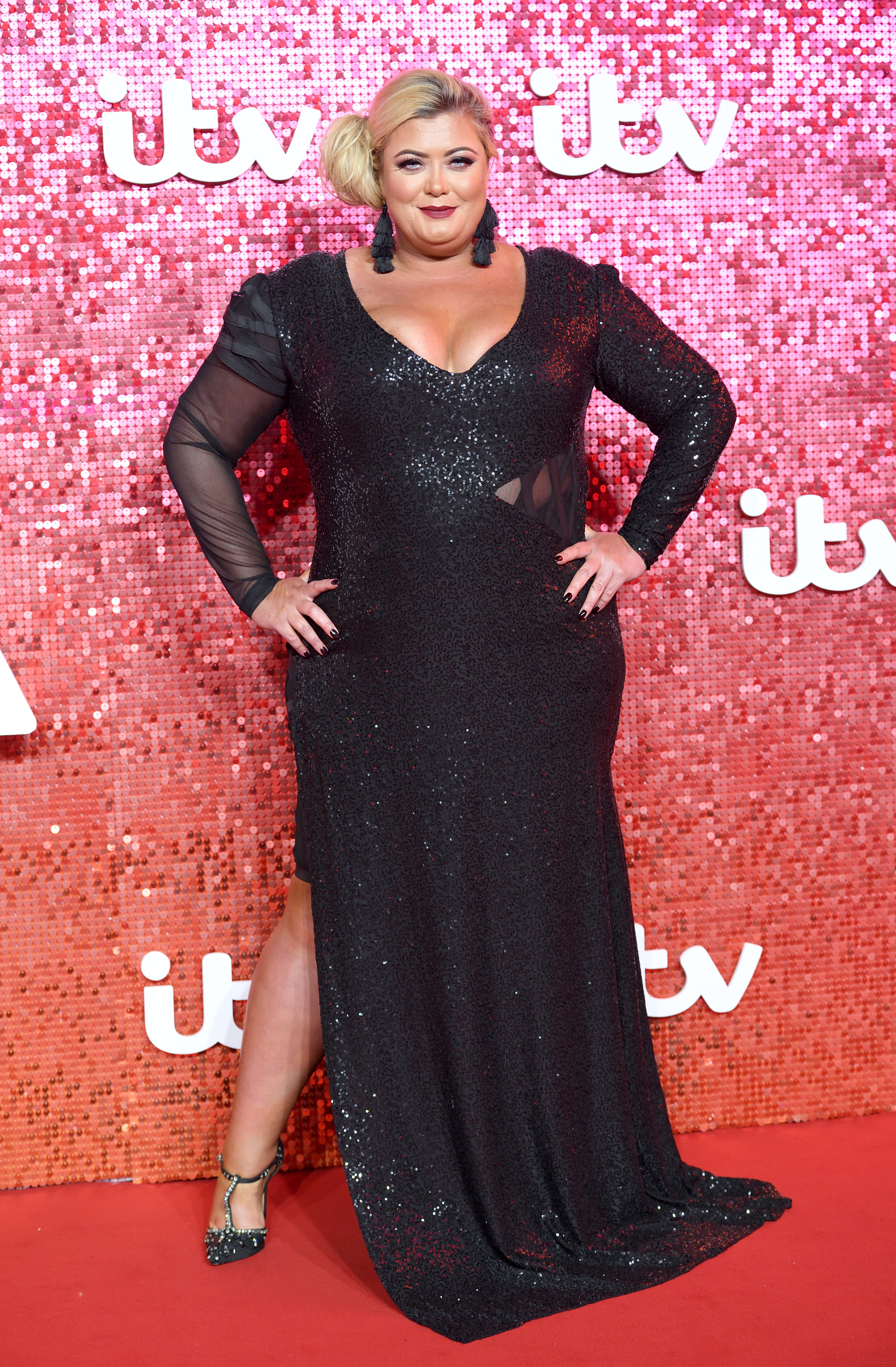 Gemma Collins attended the ITV Gala in London on November 9, 2017, making a glamorous red carpet appearance in a floor-length black sequinned gown with sheer sleeves and a thigh-high split. With her hair styled to one side and her hands confidently on her hips, Collins leaned into full evening glamour at a time when she was firmly established as a television personality.