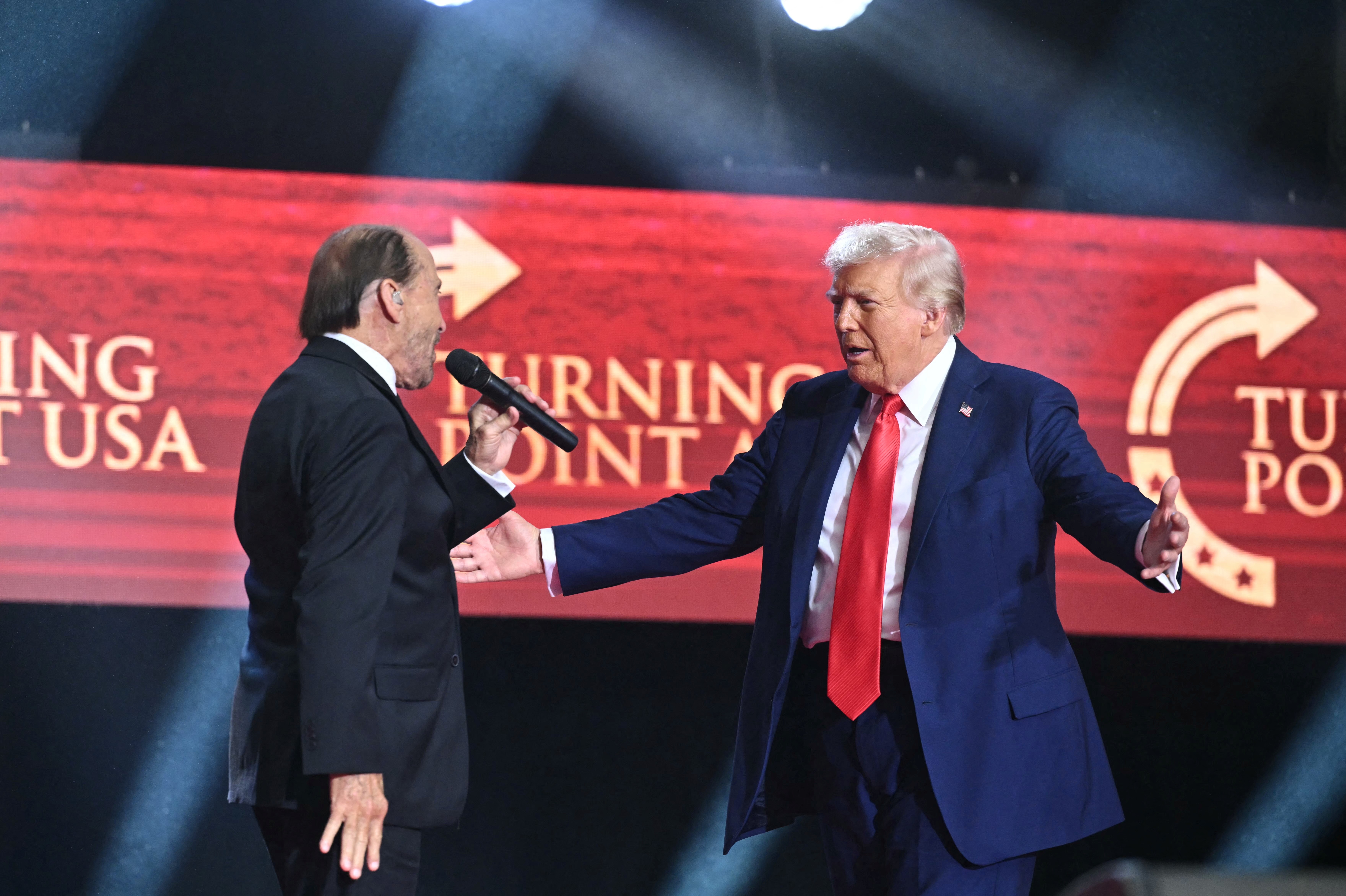Donald Trump is greeted by Lee Greenwood as he arrives to speak at the public memorial service for Charlie Kirk at State Farm Stadium on September 21, 2025, in Glendale, Arizona | Source: Getty Images