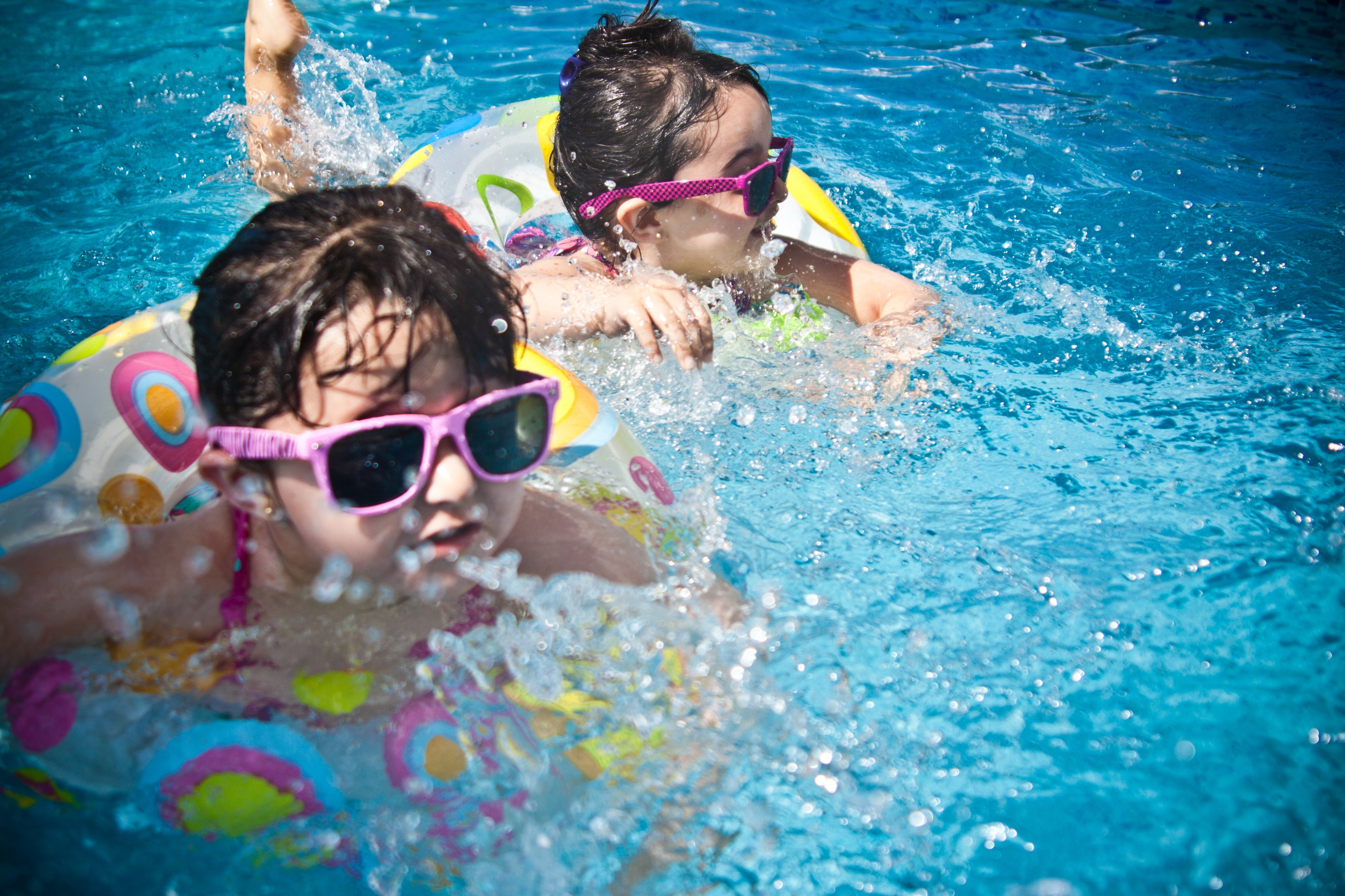 Two kids wearing sunglasses splash and swim in a pool of water | Photo: Pexels/Juan Salamanca 