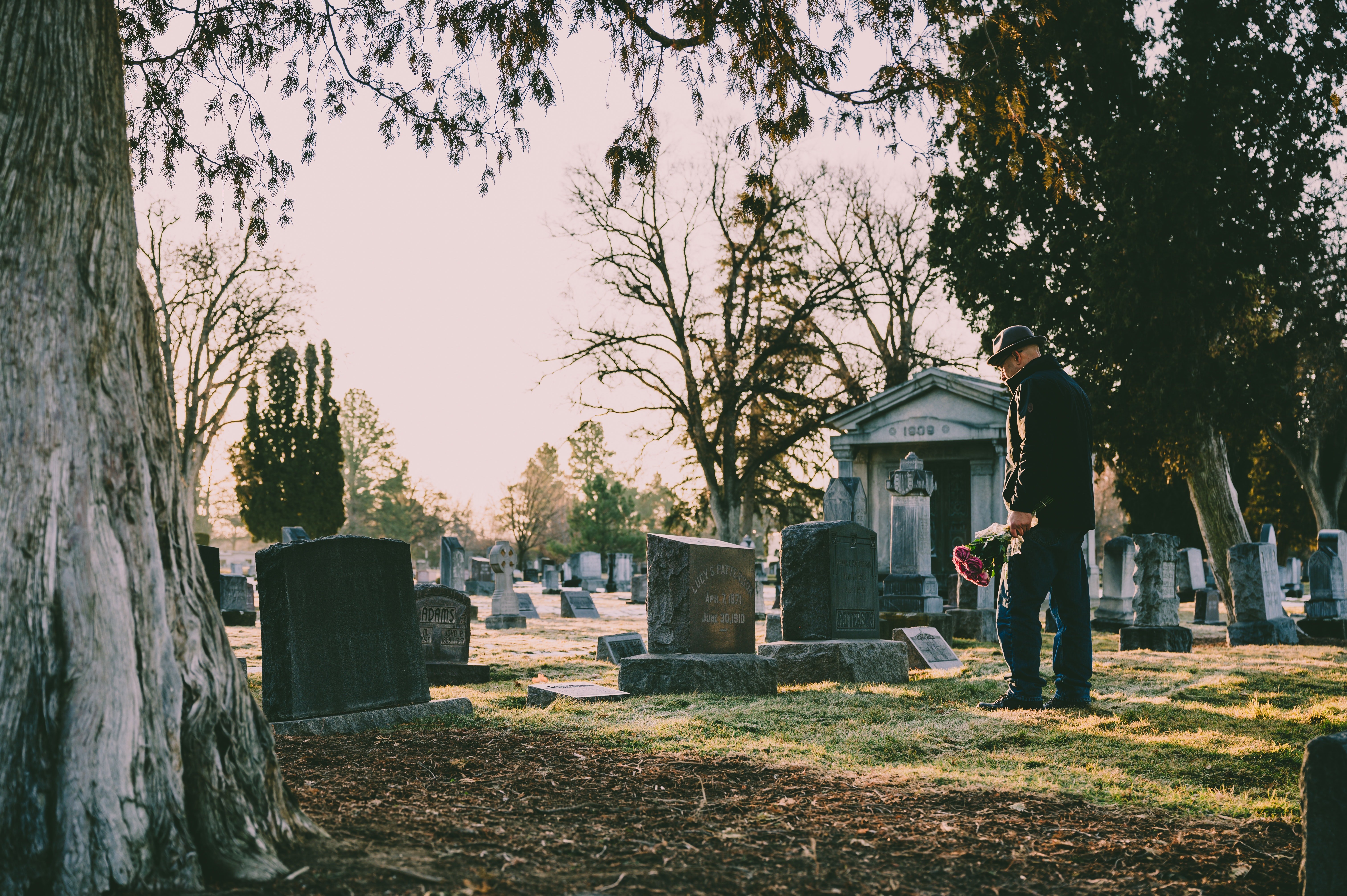 Man standing in a black jacket in front of a grave with flowers in his hand | Photo: Pexels