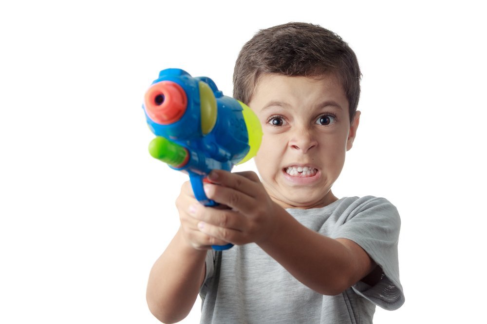 Little boy with funny expression playing with plastic water gun. | Photo: Shutterstock
