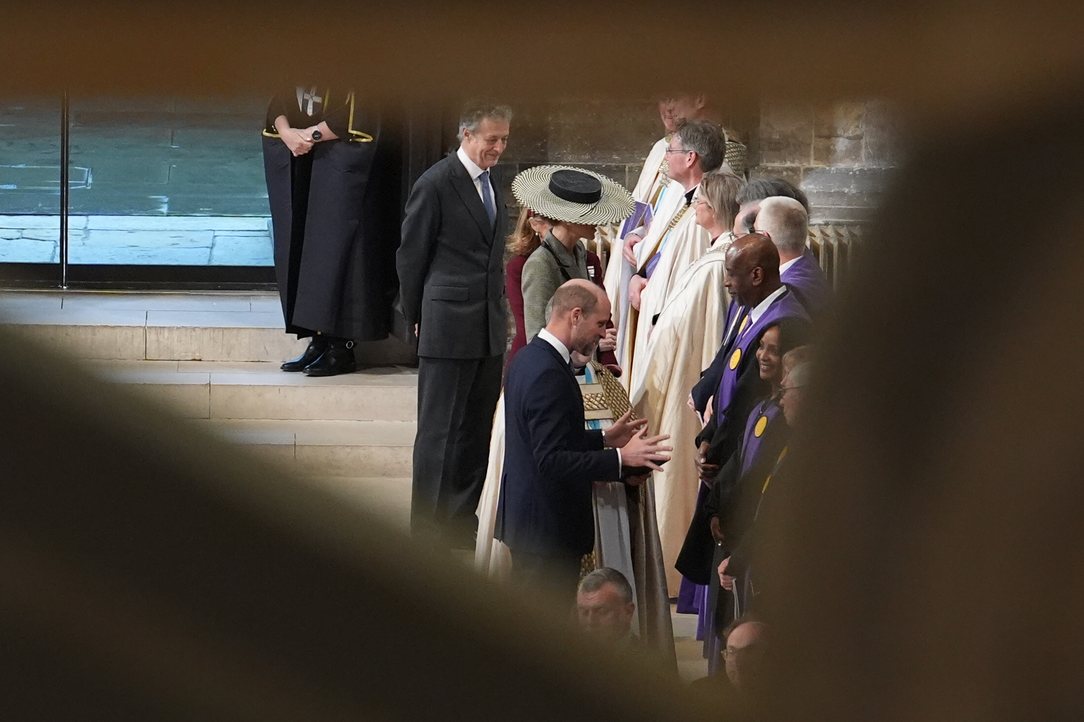 Glimpsed through the crowd, the Princess of Wales's boater hat is still unmistakable, rising above the assembled clergy in their cream and purple robes as Prince William greets one of the officiants. It is a fittingly understated view of a hat that had been anything but understated all day — now quietly present at the heart of a ceremony that made history.