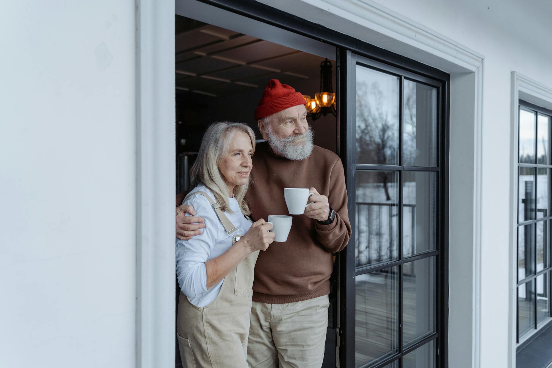 An older couple standing at a doorstep, each holding a cup | Source: Pexels