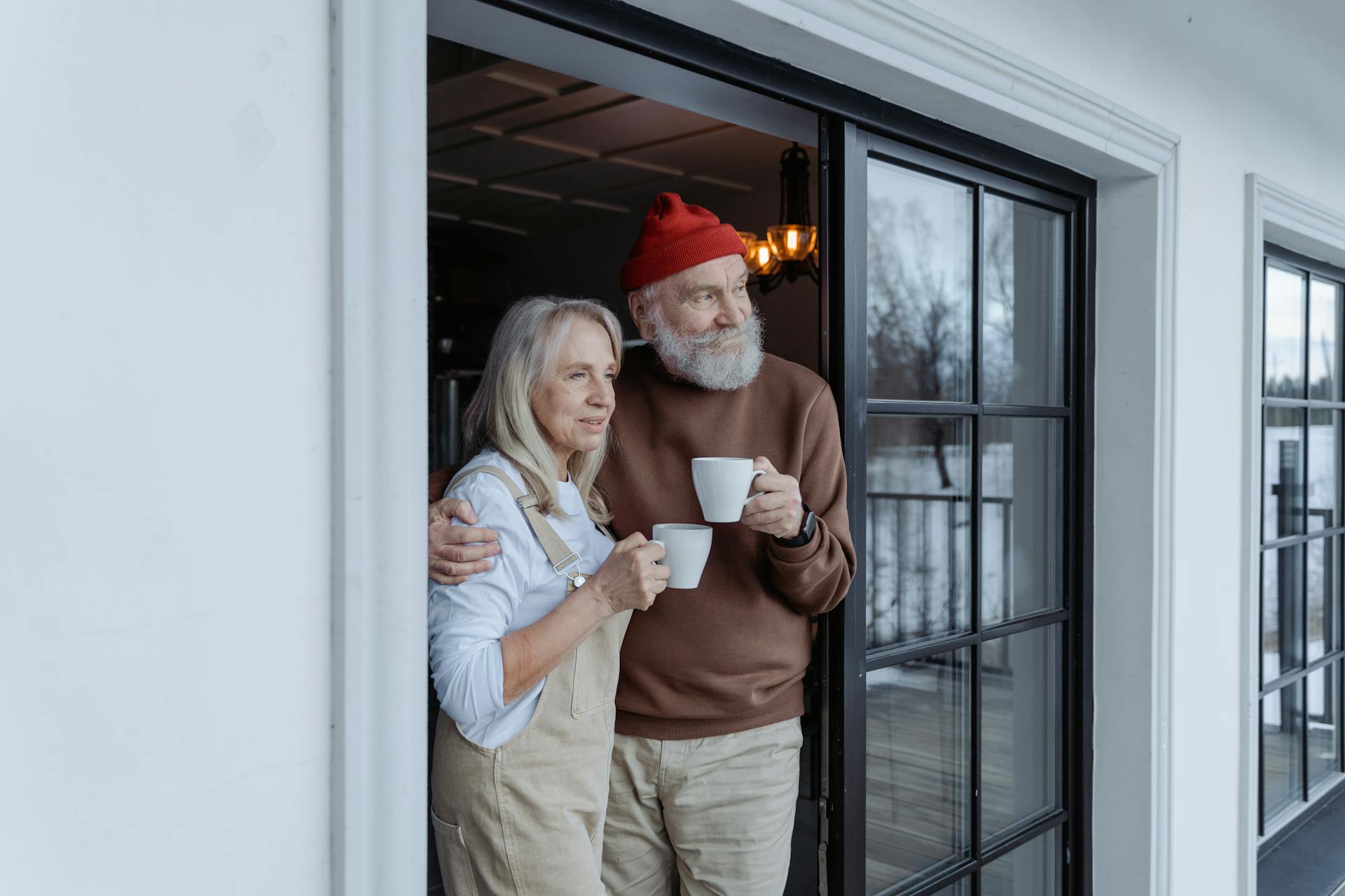 Um casal mais velho parado na porta, cada um segurando uma xícara | Fonte: Pexels