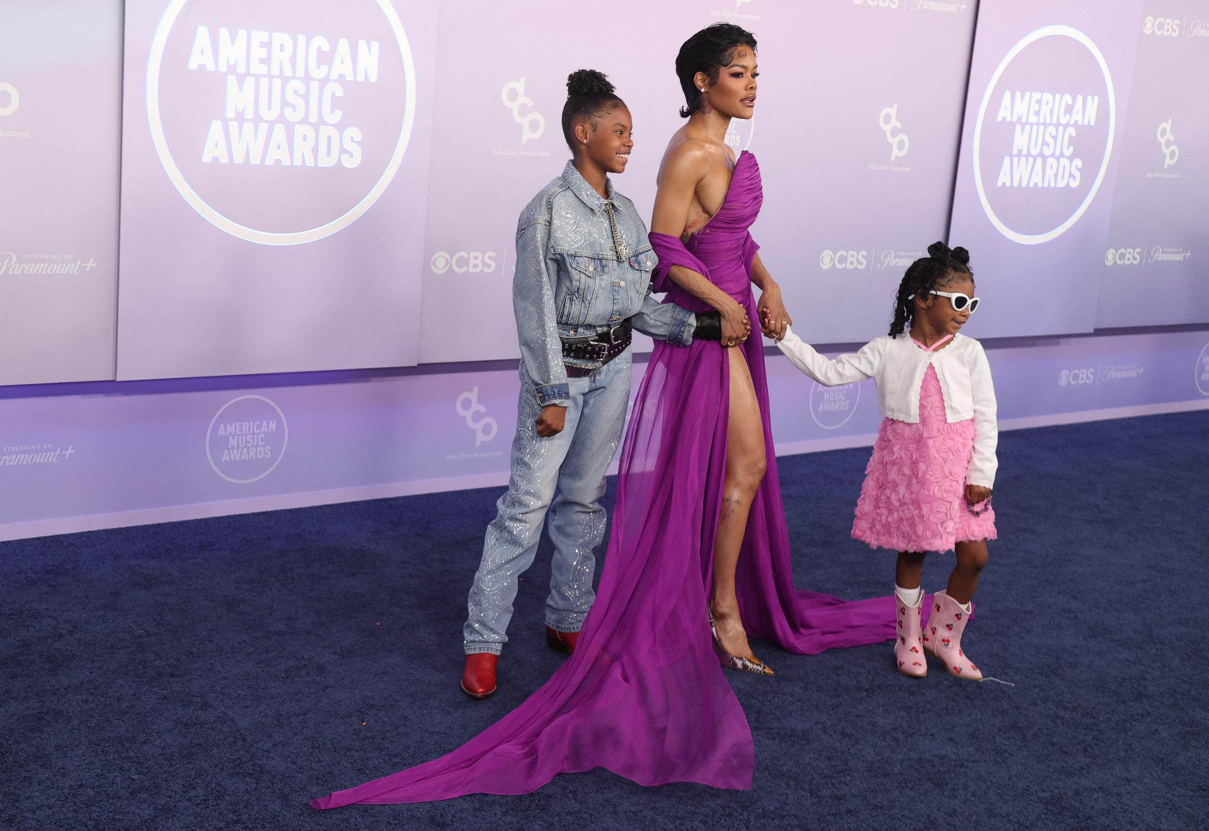 Teyana Taylor walks hand in hand with her daughters, who arrived in sparkling denim, red boots, pink layers, and oversized white sunglasses | Source: Getty Images
