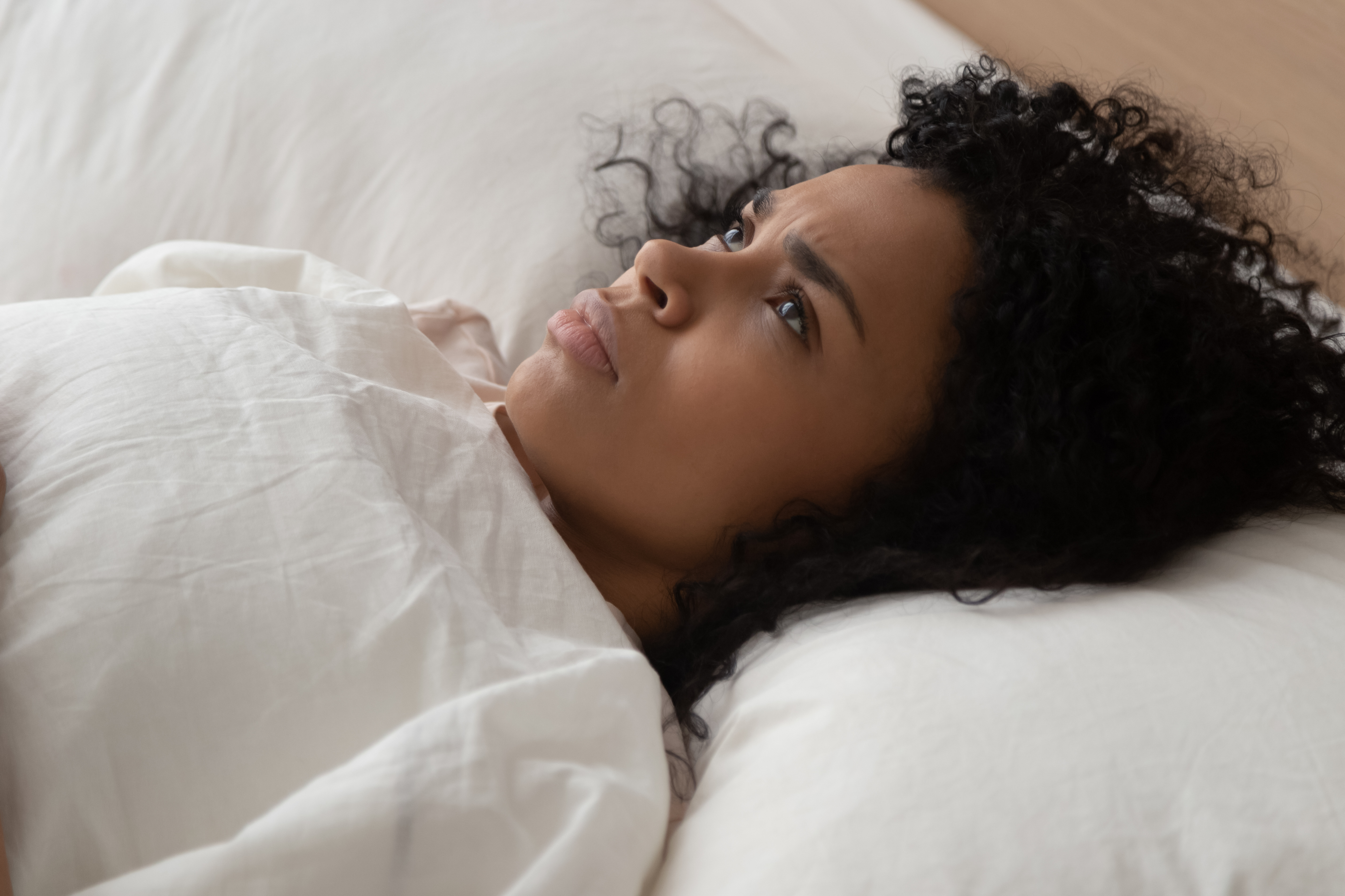 A black woman facing up while having trouble falling asleep | Source: Shutterstock