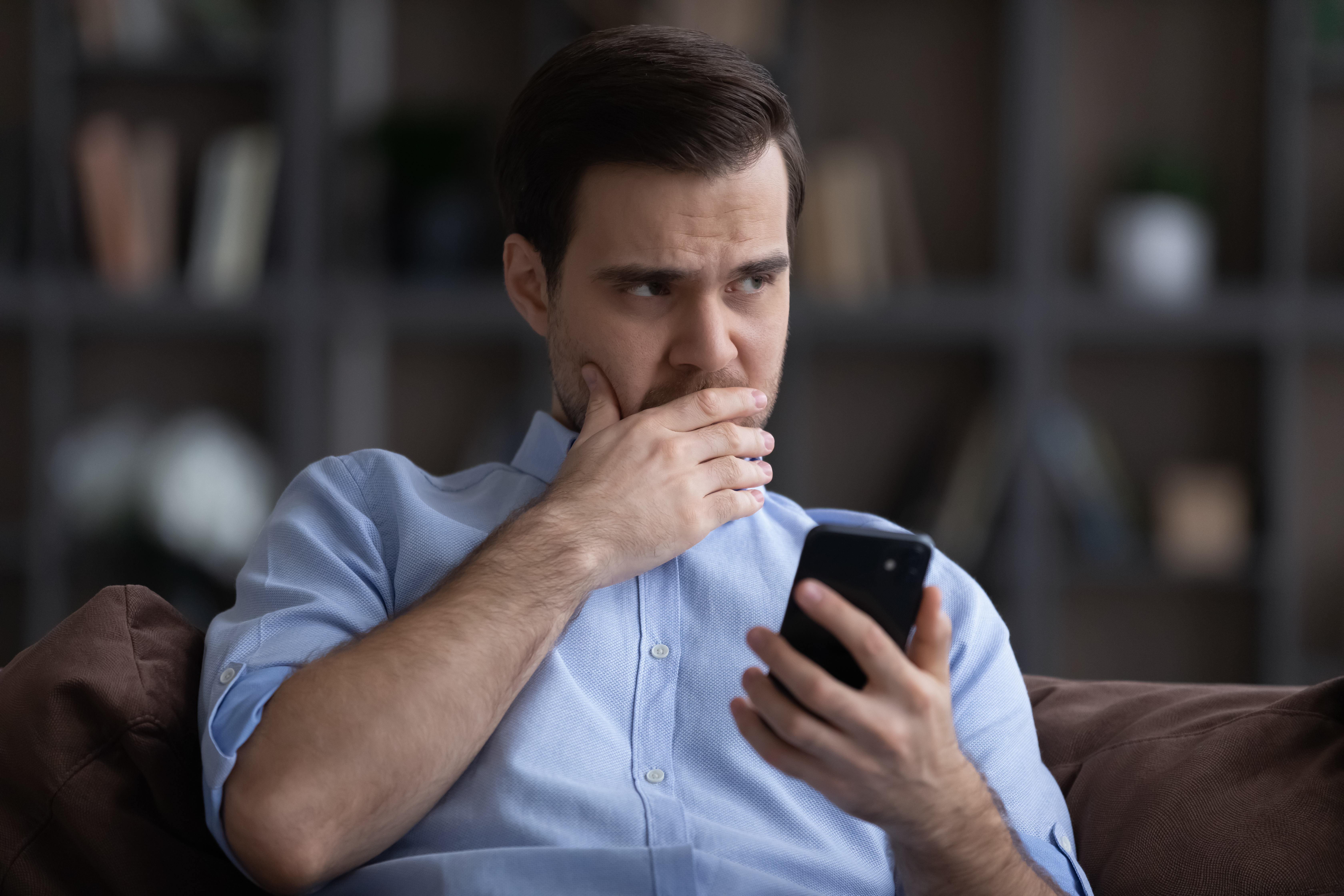 An anxious man thinking while holding his phone | Source: Shutterstock