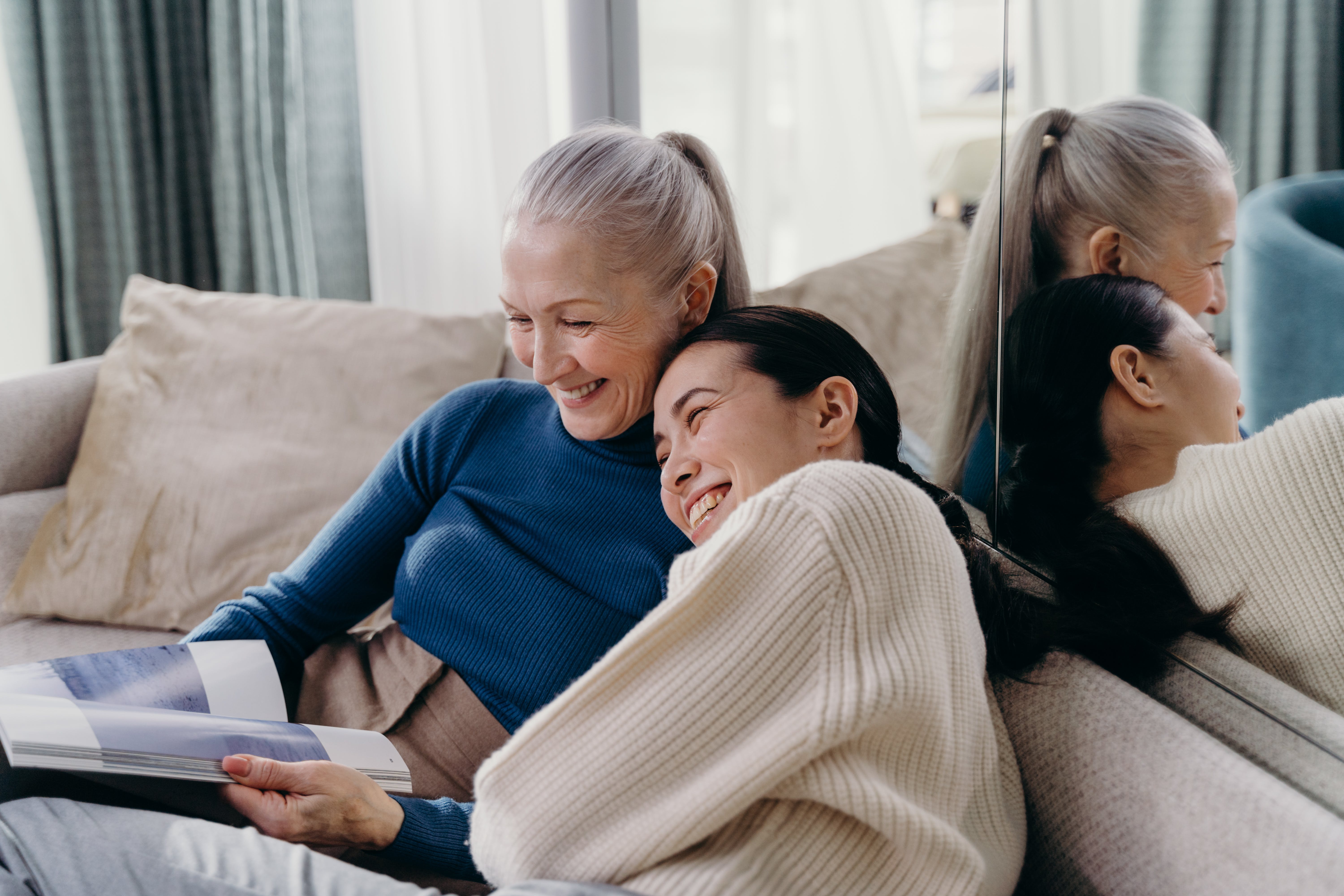 An elderly woman laughing with a young woman on the couch | Source: Pexels