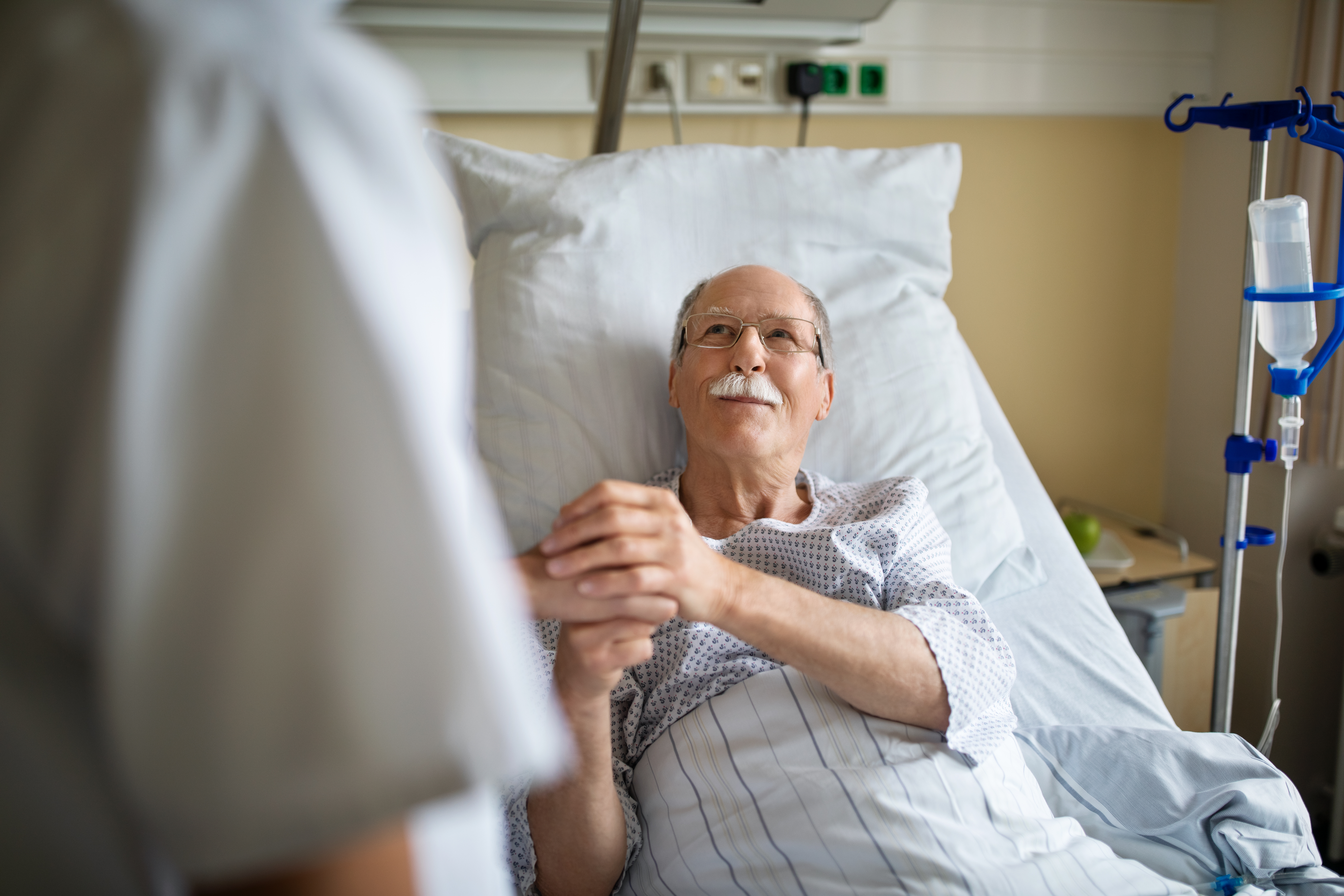 Senior man holding hand of female nurse in hospital room | Source: Getty Images