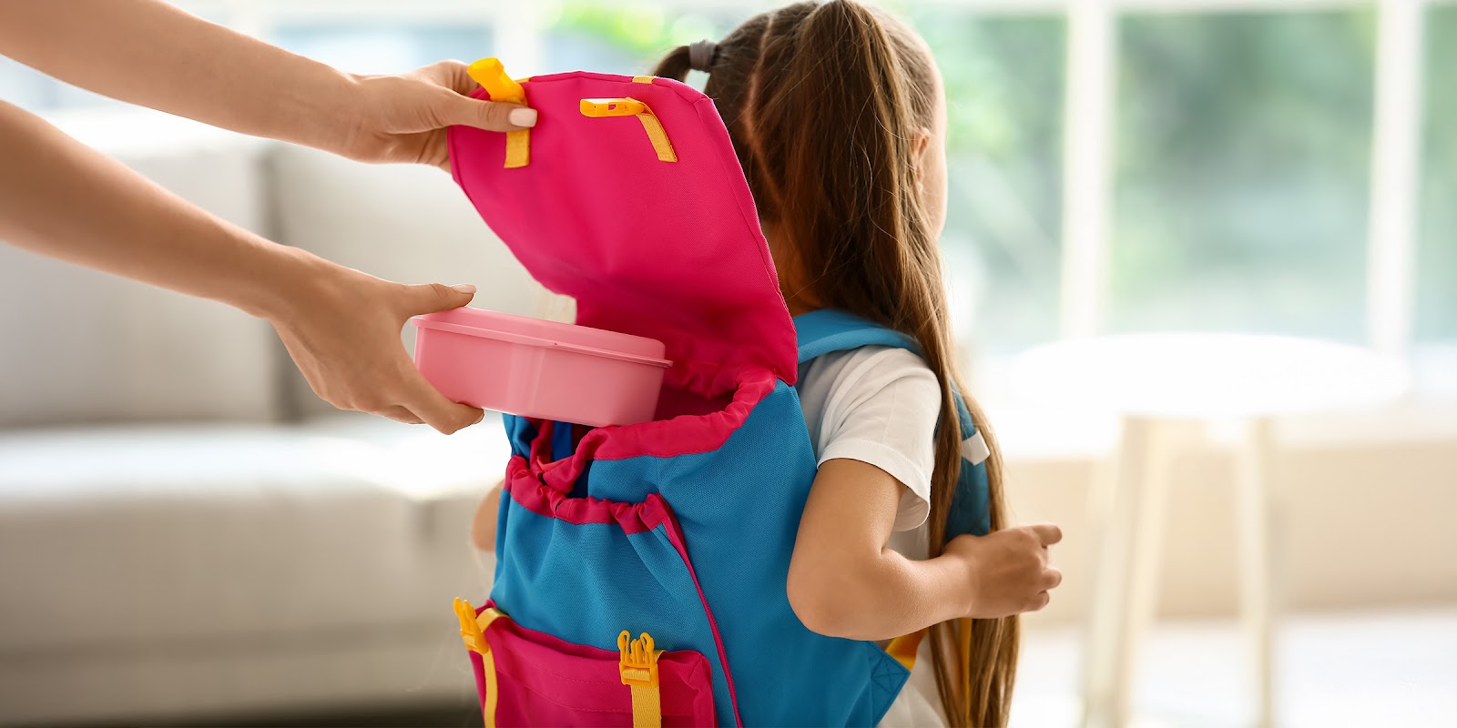 An adult placing a lunchbox into a child’s backpack | Source: Shutterstock