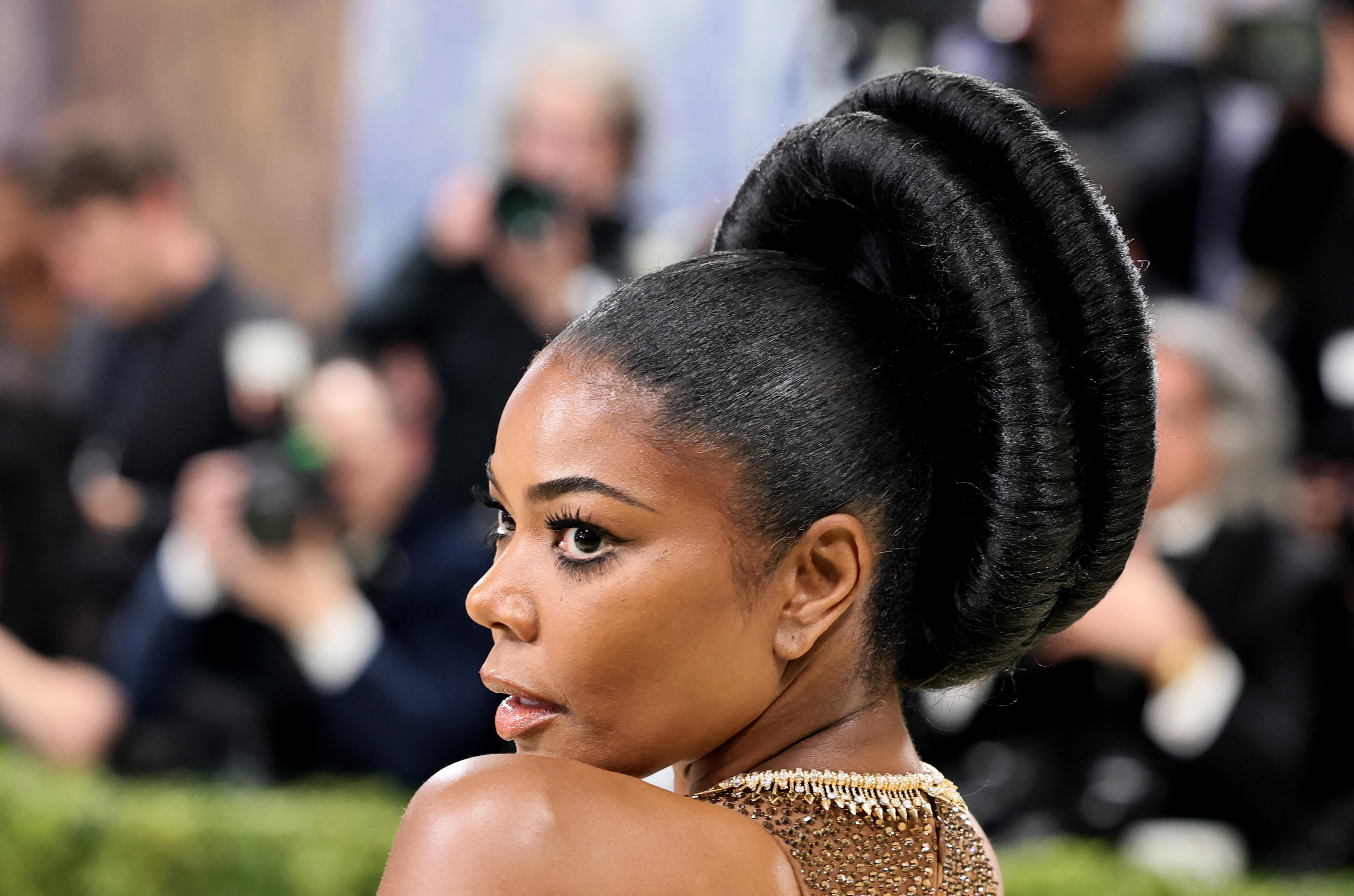 Gabrielle Union turns over her shoulder in a glittering bronze gown with a daring open-back design. Her sleek, sculpted updo and soft glam makeup add a polished, red-carpet finish.