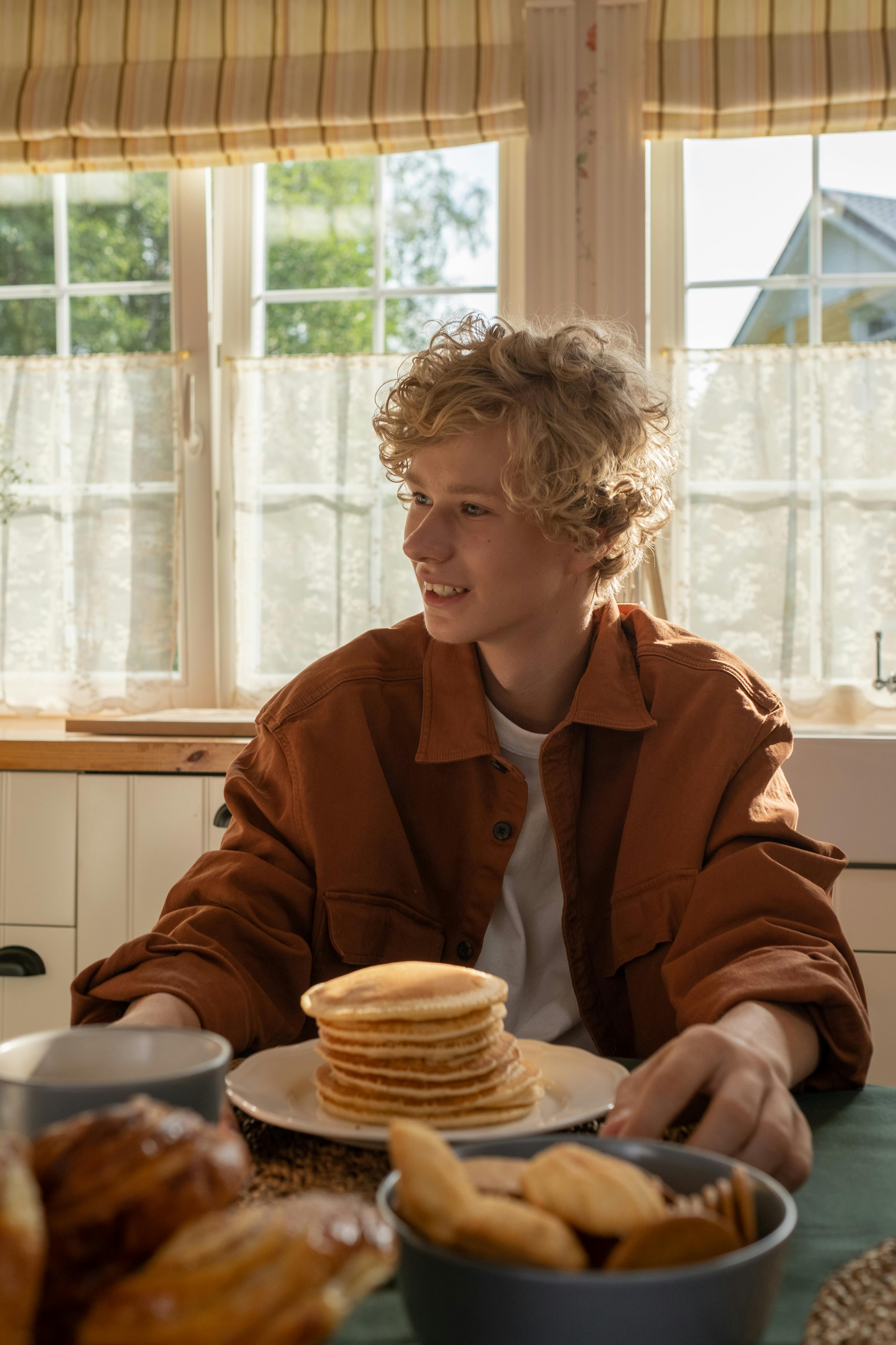 A smiling boy sitting at the table with pancakes in front of him | Source: Pexels