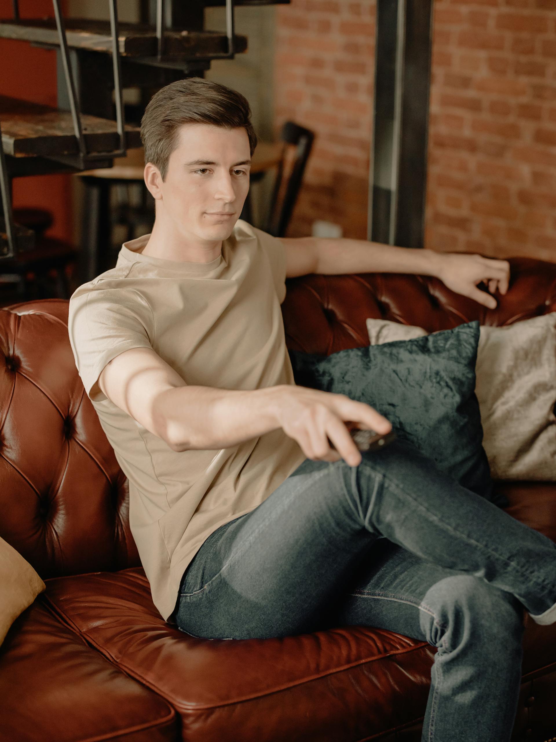 A man sitting on a sofa with a remote on his hand | Source: Pexels