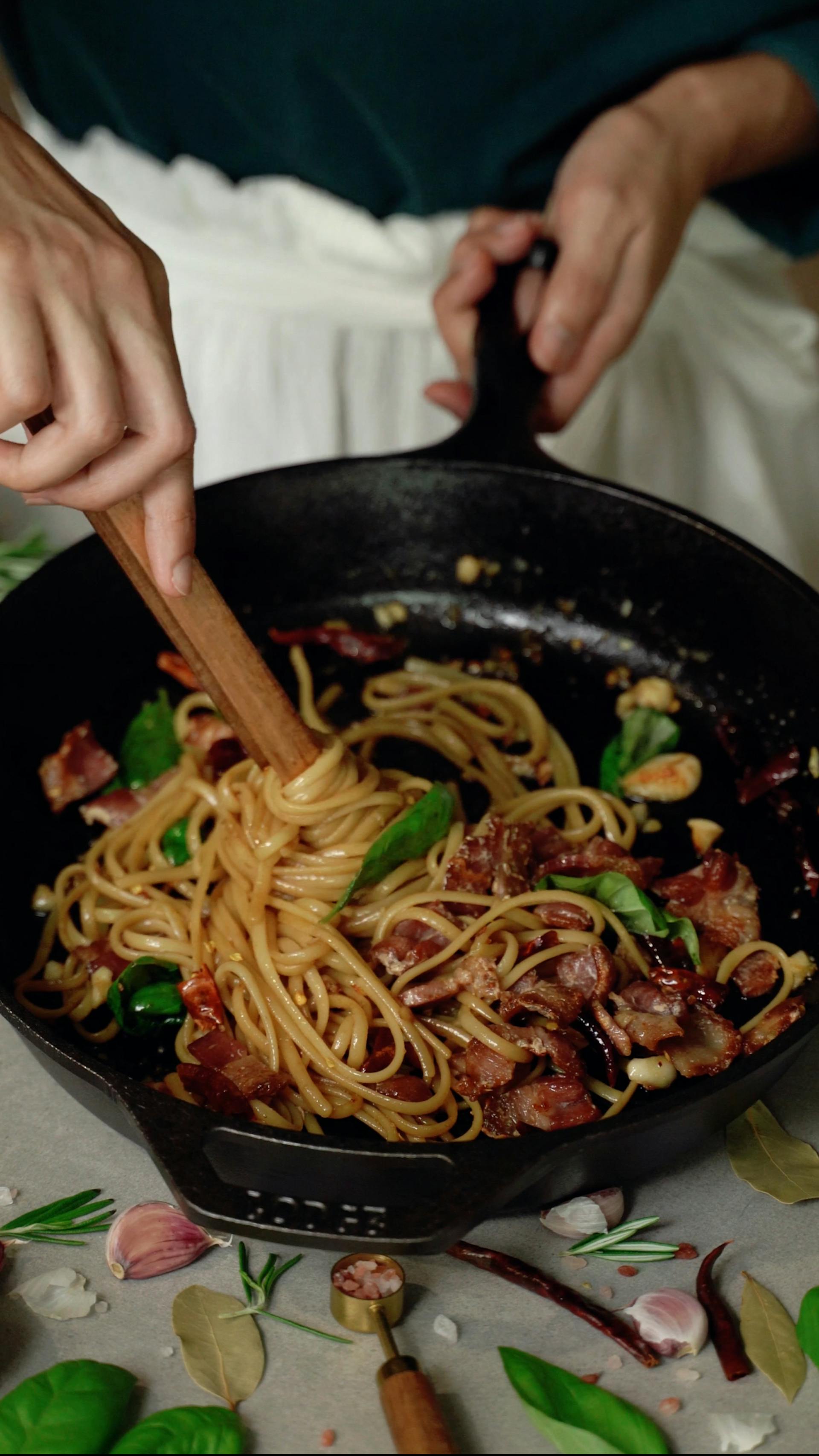 A closeup of a woman tossing spaghetti in a pan | Source: Pexels