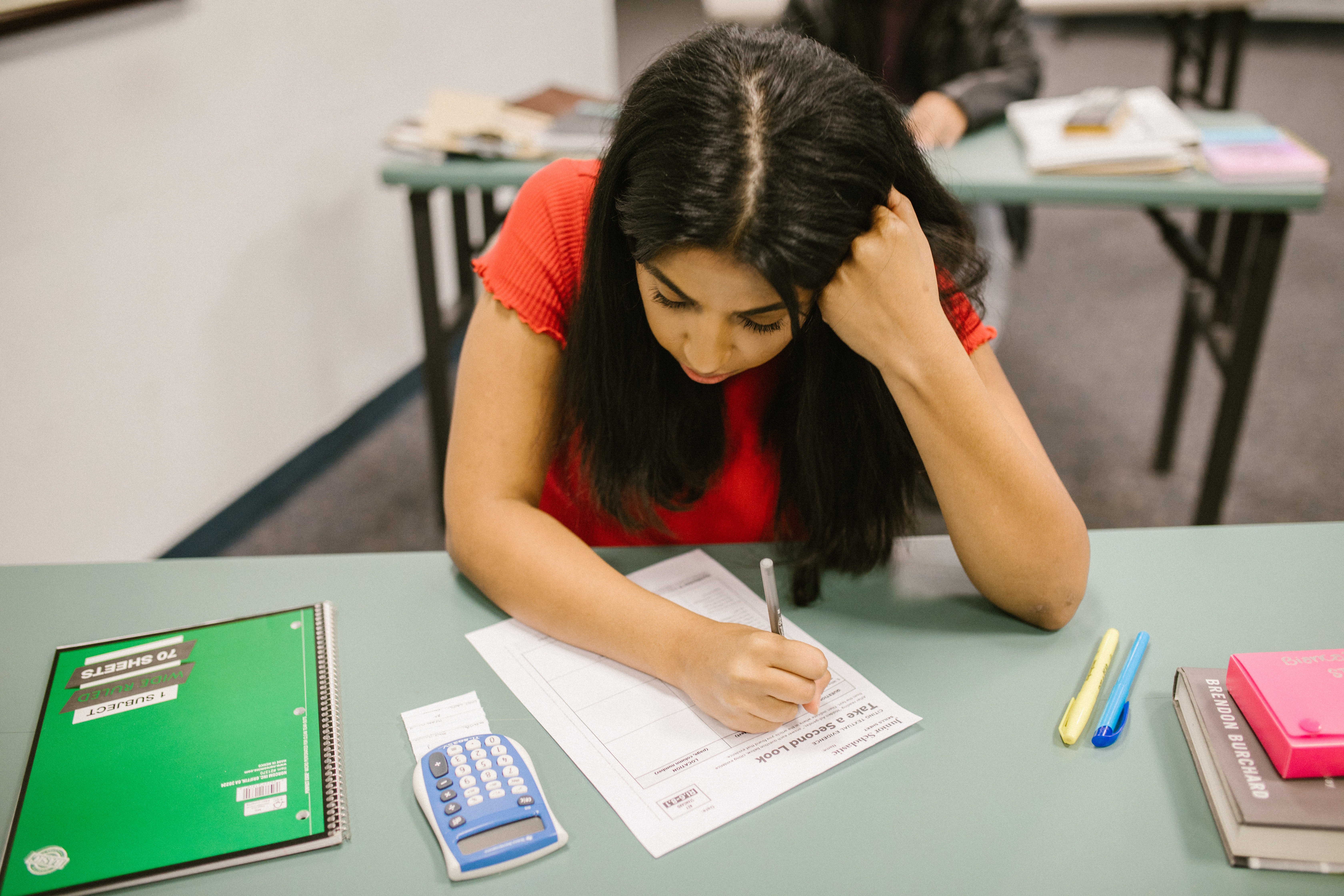 A female student writing a test with a calculater on her desk. | Pexels/ RODNAE Productions