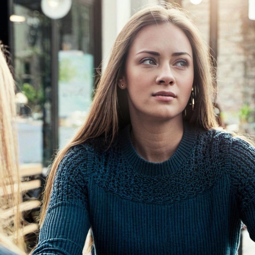 A woman talking to another at a café table | Source: Midjourney