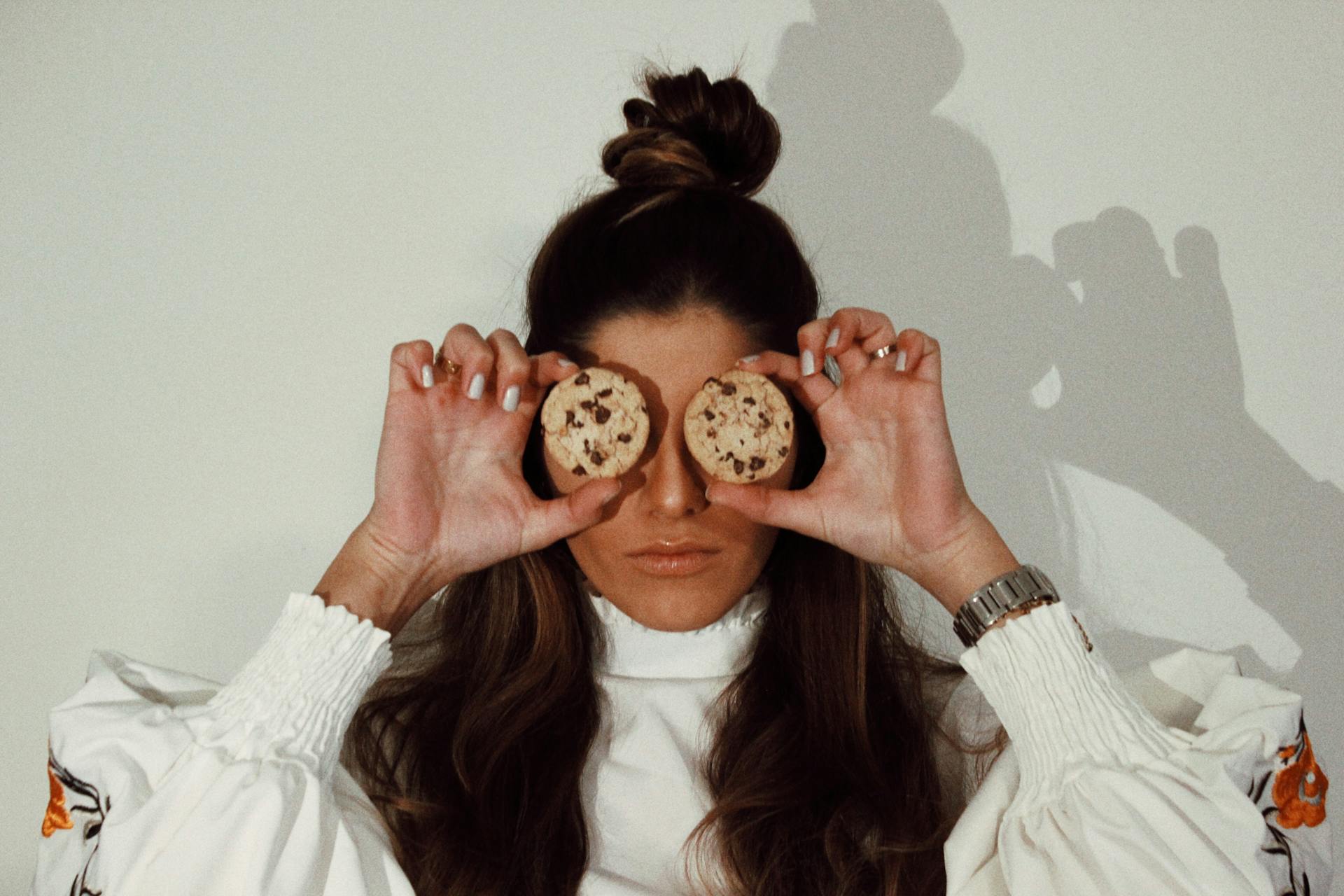 A woman covering her eyes with two chocolate chip cookies | Source: Pexels