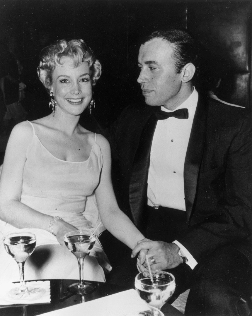 Married American actors Barbara Eden and Michael Ansara holding hands while seated at a table with cocktails in formal attire. | Source: Getty Images