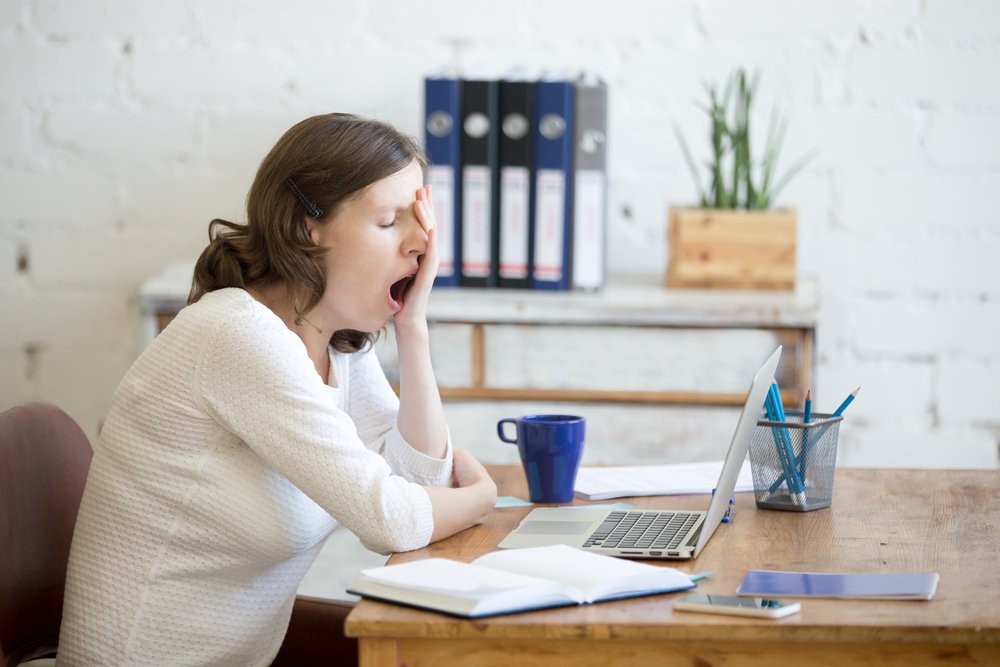 Une jeune femme assise en face d'un ordinateur portable, endormie, fatiguée. | Shutterstock