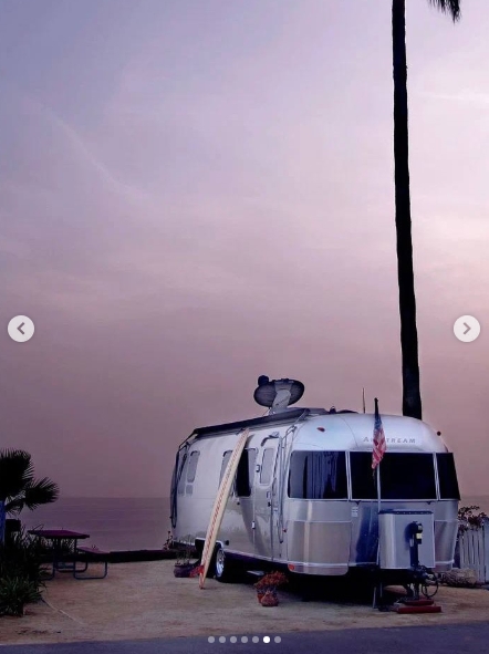 Parked beside the ocean beneath a towering palm tree, the Canoe showed why McConaughey was drawn to a home that could change addresses whenever he wished. The Airstream's recognizable curved aluminum shell sat against a coastal backdrop, complete with a rooftop satellite dish and an American flag, while a surfboard rested alongside it ready for another day near the water. | Source: Instagram/ivd_ru