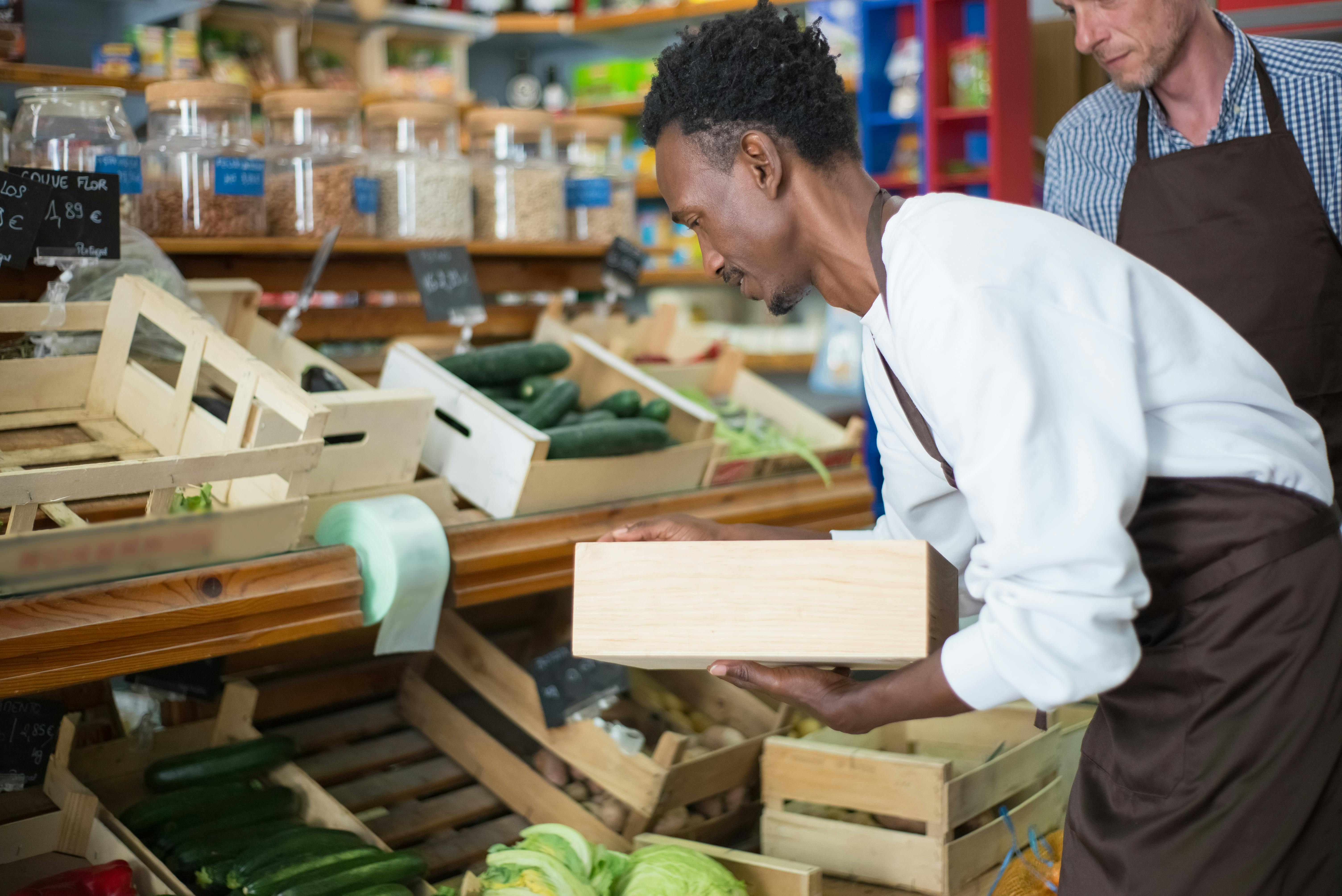 A shop worker carefully stocks fresh produce while another staff member looks on. | Source: Pexels