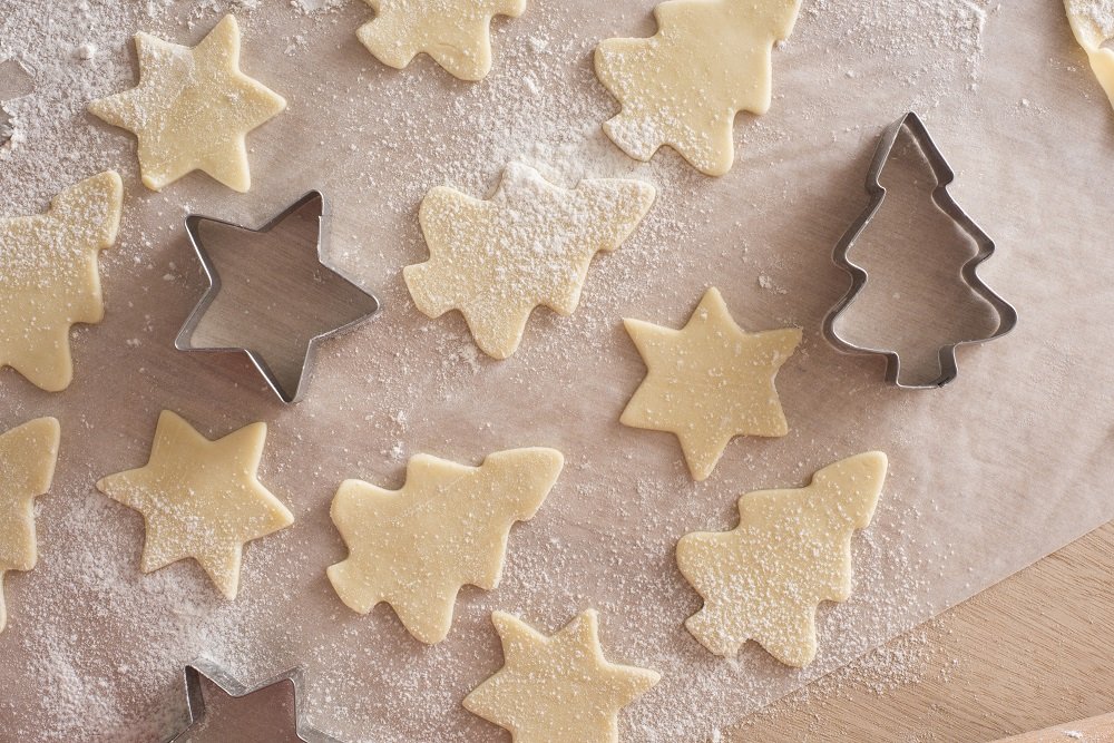 Making Christmas cookies with star and tree-shaped cookie cutters in an overhead view of uncooked pastry shapes on oven paper | Photo: Freeimageslive/christmashat